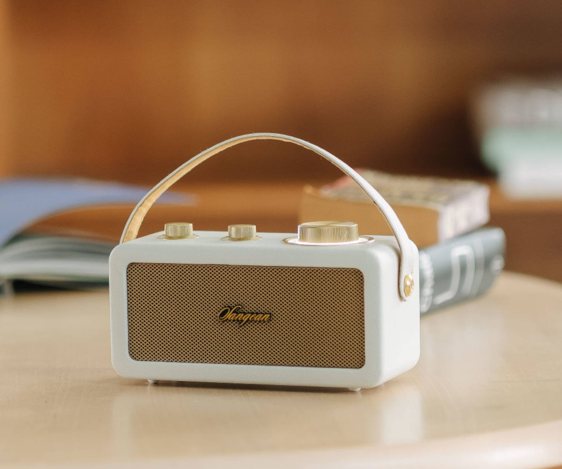 Altavoz blanco y dorado de estilo retro sobre mesa de madera, libros detrás.