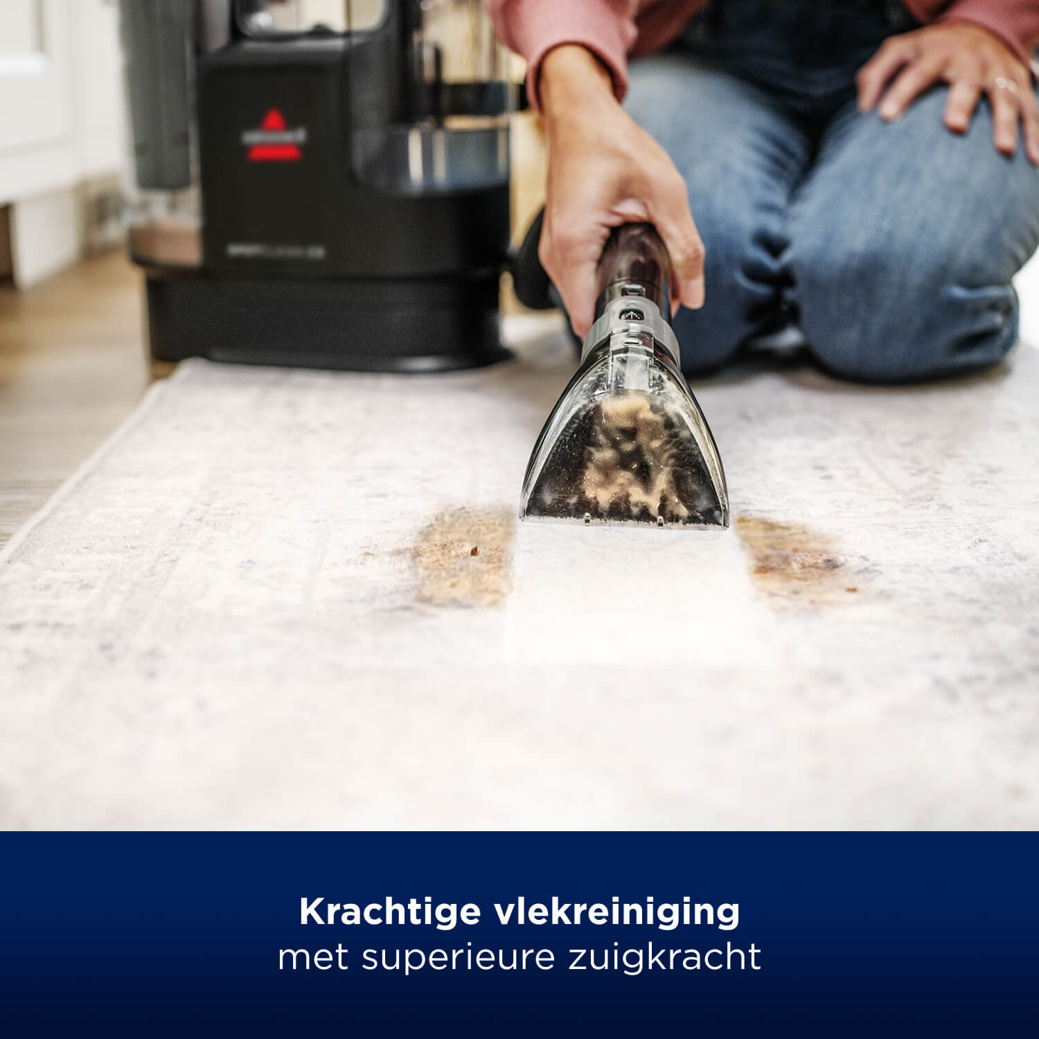 Eine Person benutzt ein Reinigungswerkzeug auf einem Teppich. Der Teppich ist hell und fleckig.