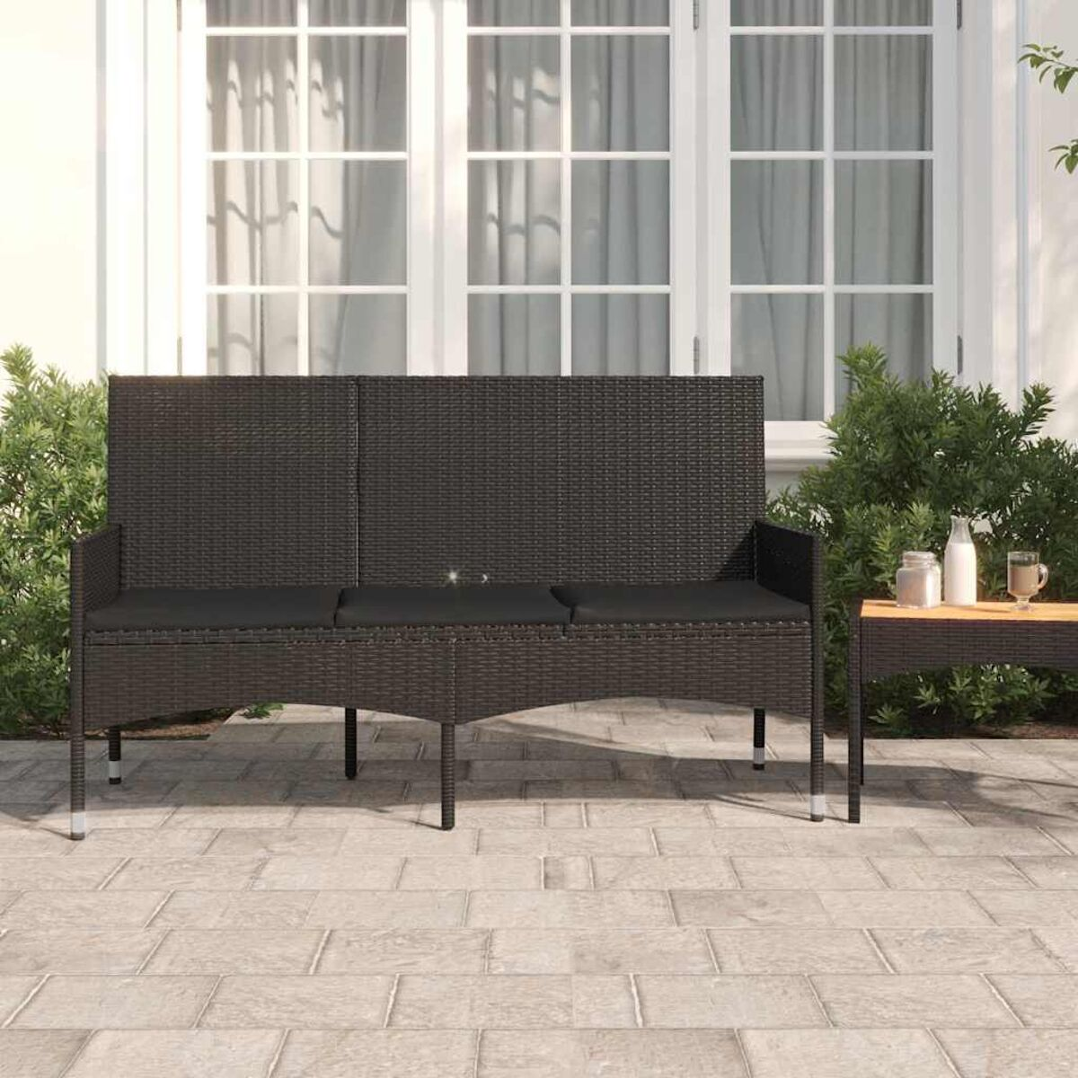 Schwarzes Korbmöbel-Sofa auf einer Terrasse, mit kleinem Tisch und Pflanzen im Hintergrund.