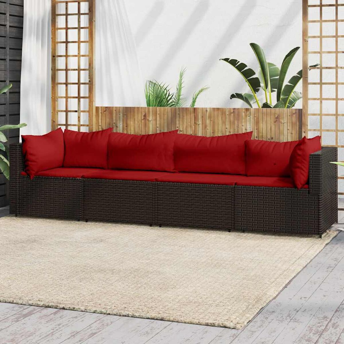 Outdoor-Wickersofa mit roten Kissen auf beigem Teppich, Holzzaun im Hintergrund.