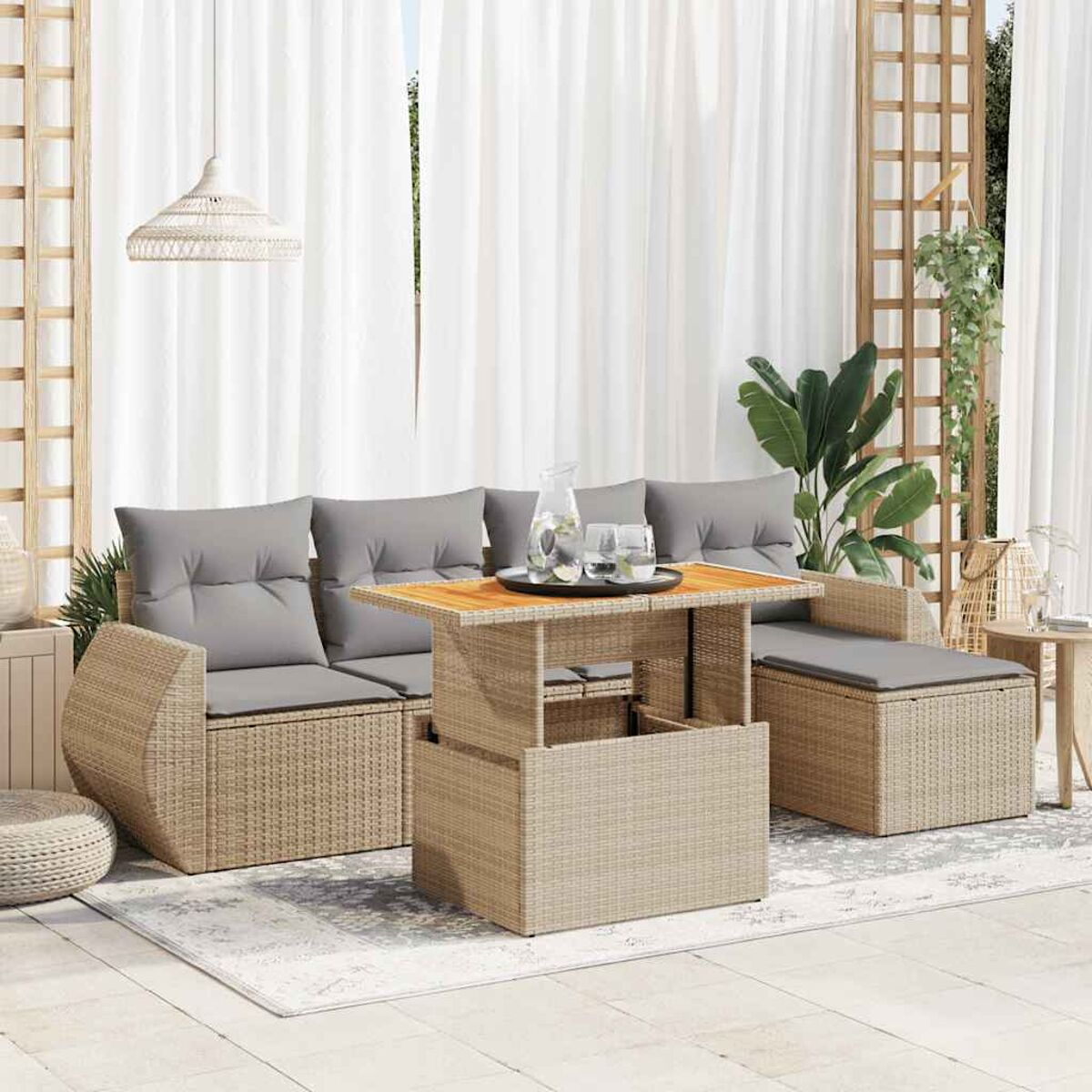 Set di mobili da patio in rattan, tavolo con bicchieri, cuscini grigi e tende bianche.
