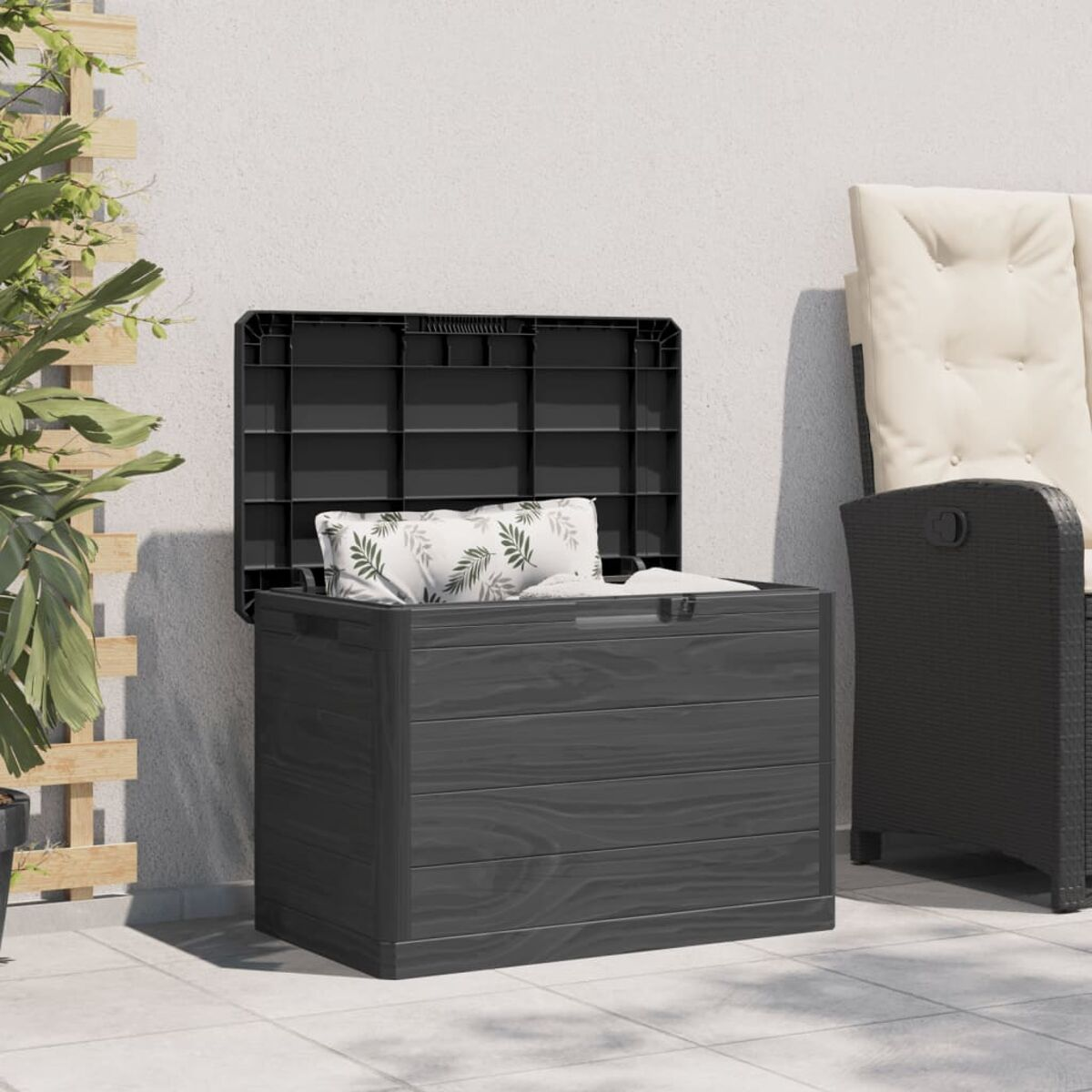 Dunkelgraue Outdoor-Aufbewahrungsbox mit offenem Deckel, ein Kissen darin. Rechts ist ein Stuhl.