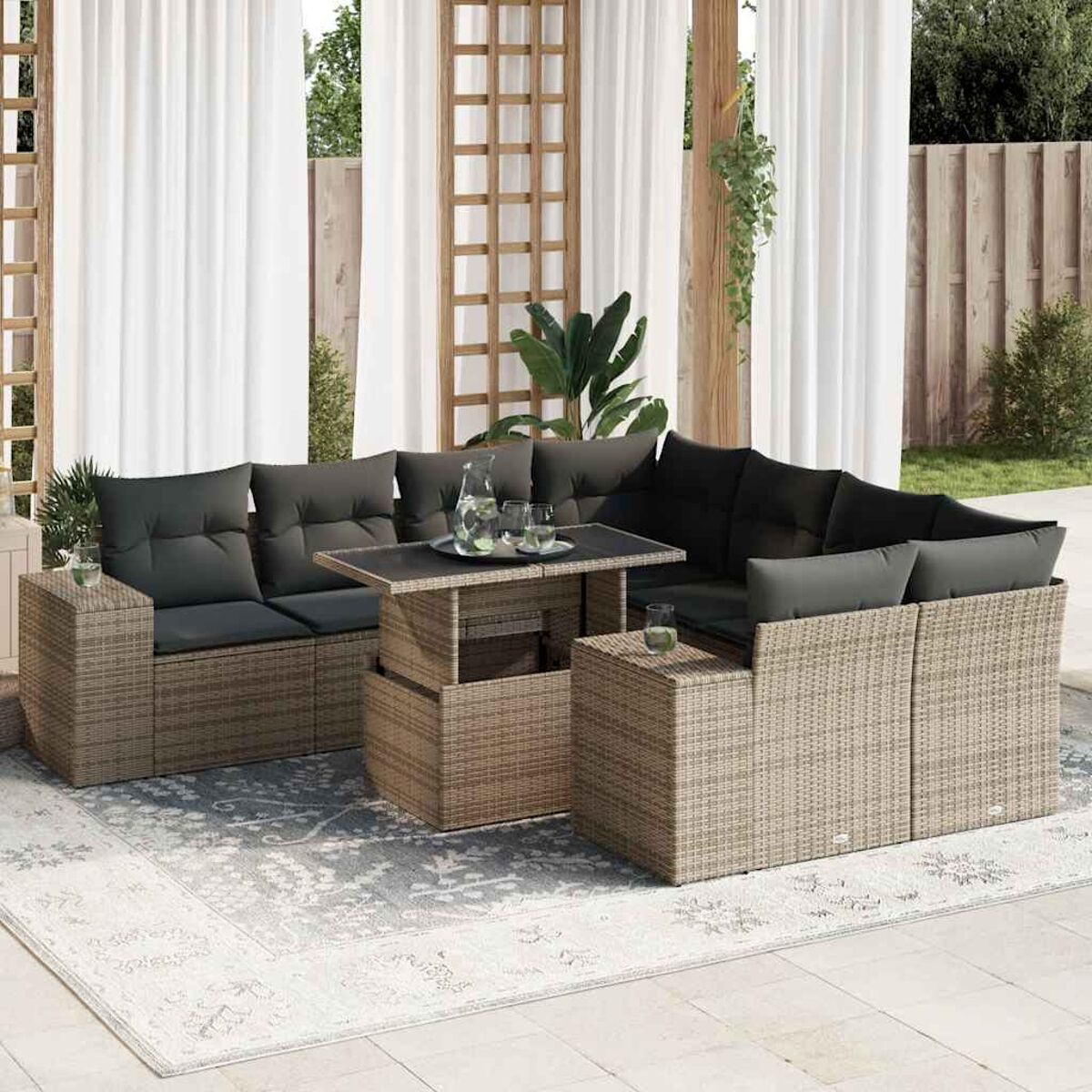 Set divano in rattan da esterno con tavolo, cuscini e tende. Su un tappeto fantasia.