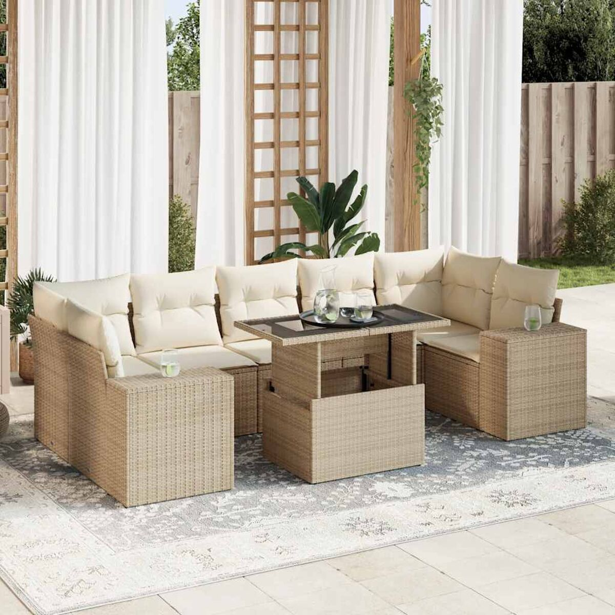 Divano esterno in vimini beige con cuscini beige e un tavolo su un tappeto fantasia, tende sullo sfondo.