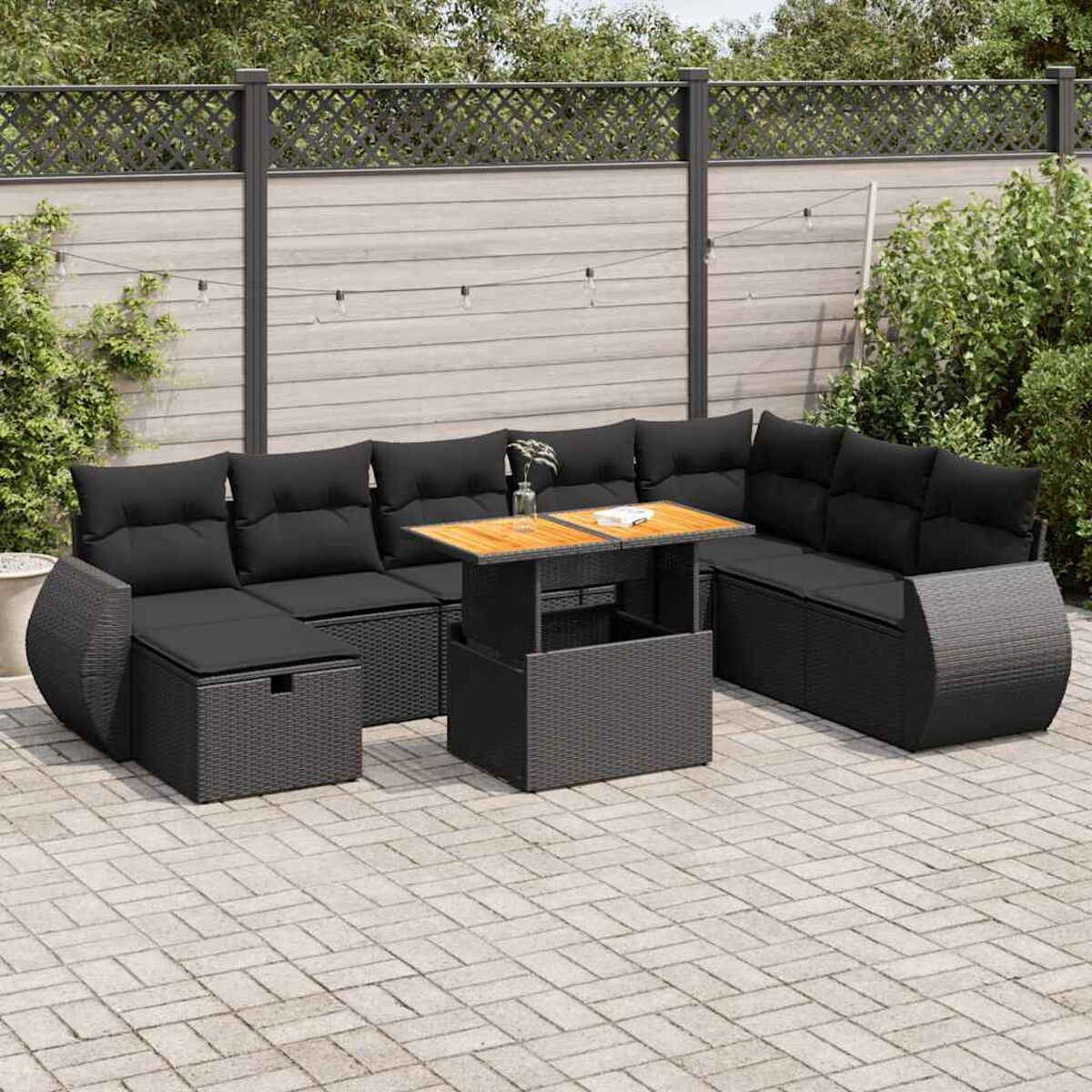 Outdoor-Set aus schwarzem Korbgeflecht auf einer Terrasse. Es umfasst ein Sofa, einen Tisch und eine Fußstütze.
