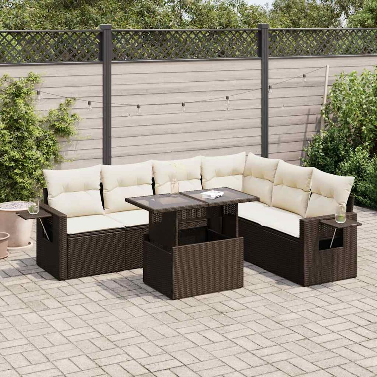 Garten-Rattan-Sofagarnitur mit Tisch, Lichterkette und Pflanzen auf einer Stein-Terrasse.