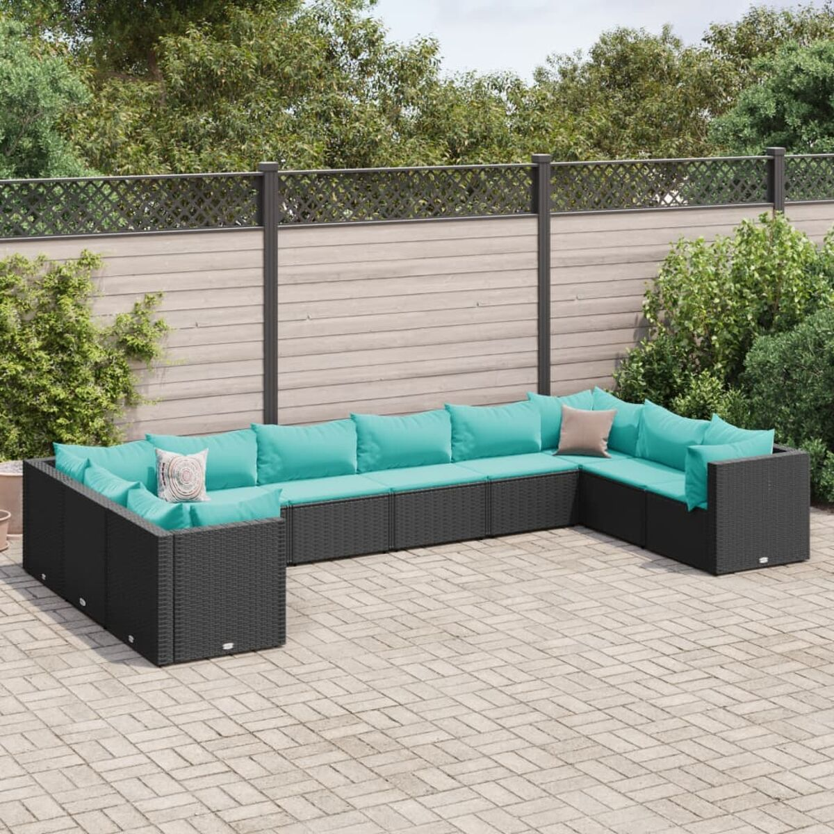 Seccional exterior de mimbre negro con cojines turquesa. Patio de ladrillo con arbustos verdes y cerca.