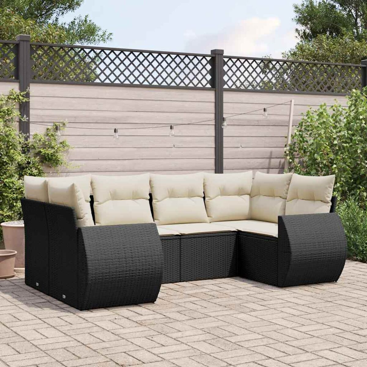 Ein schwarzes Outdoor-Sofa aus Korbgeflecht in U-Form mit cremefarbenen Kissen, auf einer Backstein-Terrasse vor einem Zaun.
