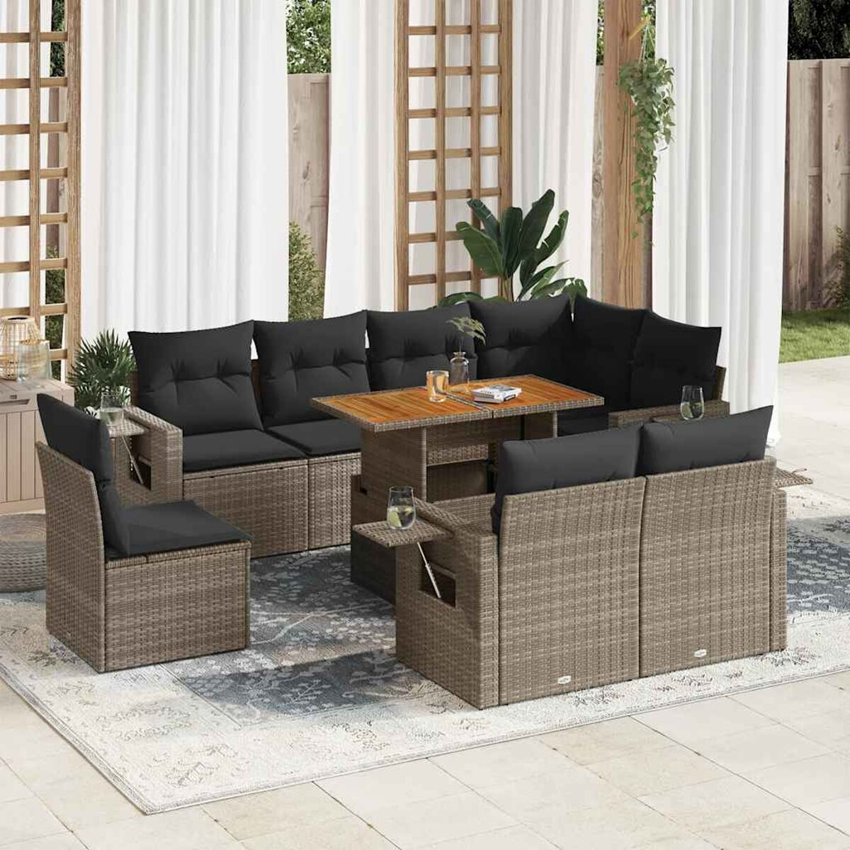Outdoor-Korbsitzgruppe mit schwarzen Kissen, einem Tisch und einem Teppich. Sonnige Szene im Freien.