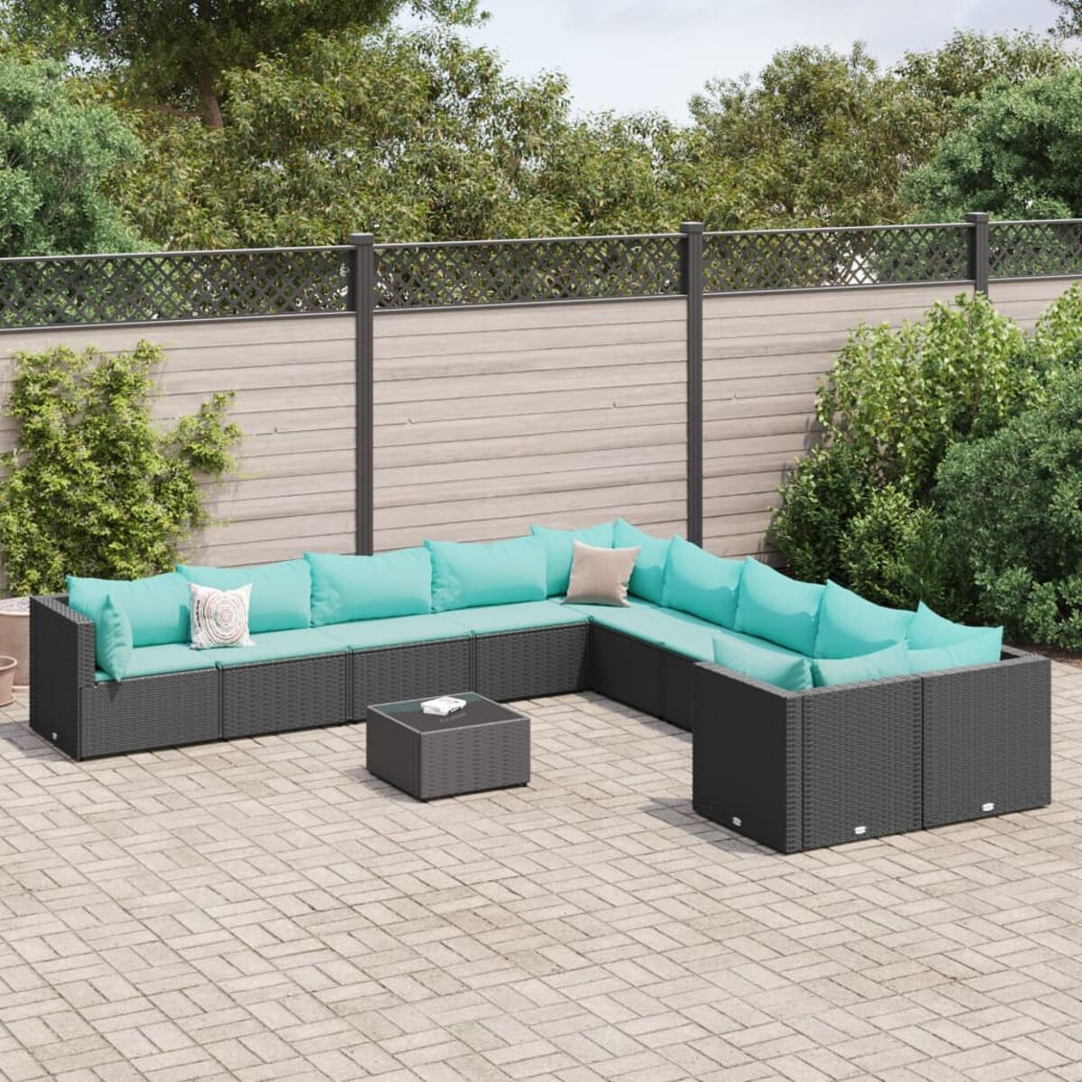 Divano componibile nero da esterno con cuscini turchesi. Su un patio in mattoni con verde sullo sfondo.