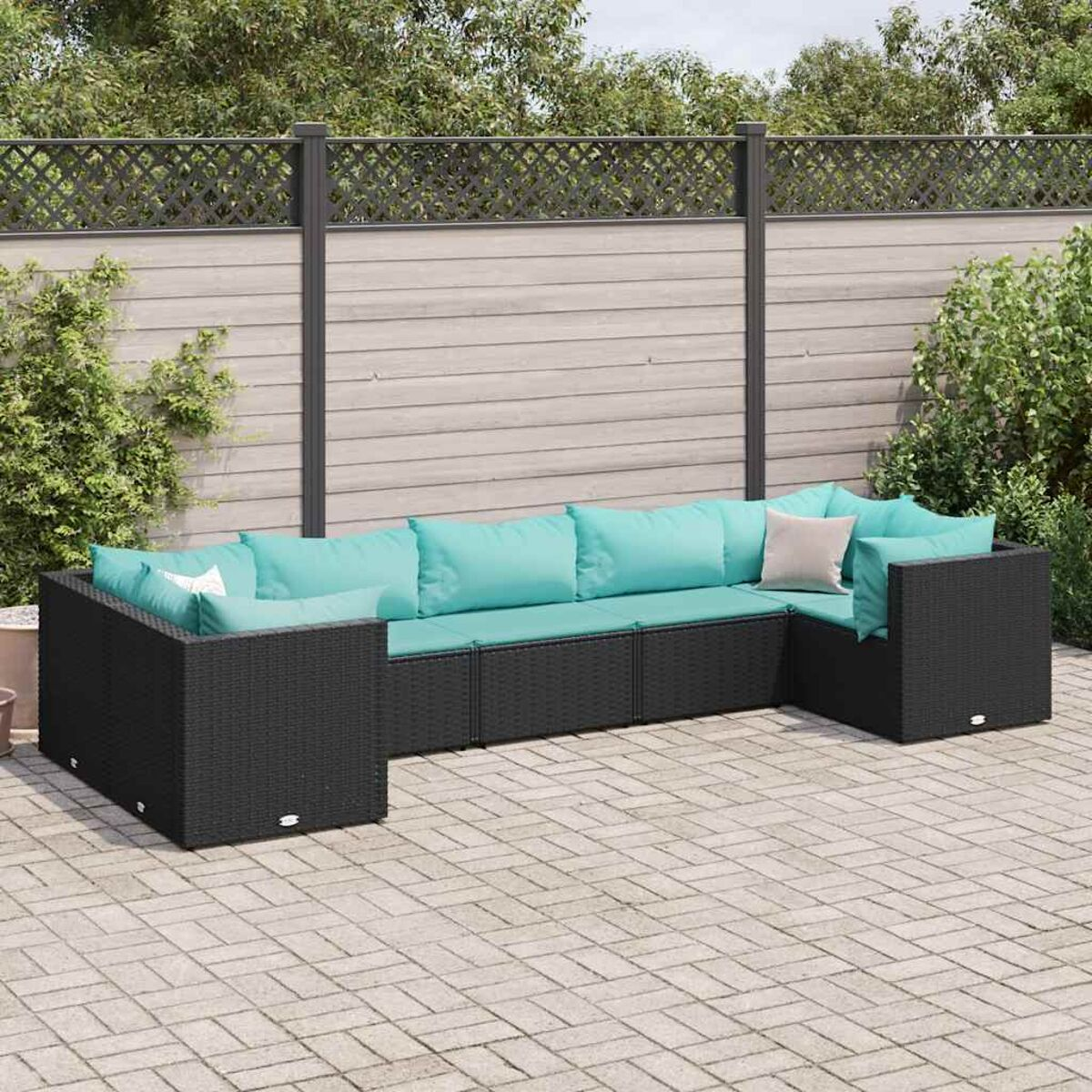 Divano componibile da esterno con cuscini turchesi, struttura nera intrecciata, su un patio in pietra, con recinzione.