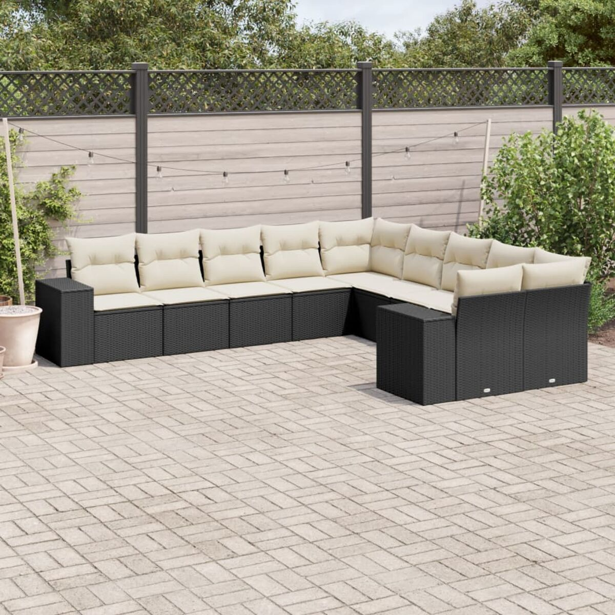 Schwarzes Outdoor-Möbelset aus Korbgeflecht auf einer Terrasse. Beige Kissen, Ziegelpflaster und Zaun.