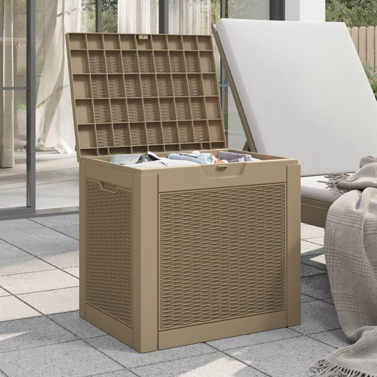 Beige Aufbewahrungstruhe mit offenem Deckel, Inhalt sichtbar. Steht auf einer Terrasse mit Sonnenliege.