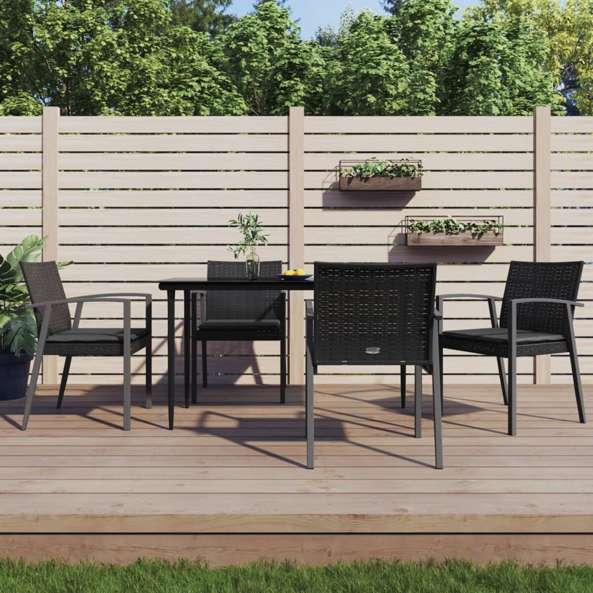 Essgruppe im Freien mit vier schwarzen Stühlen und einem schwarzen Tisch auf einer Holzterrasse, im Hintergrund ein Holzzaun.