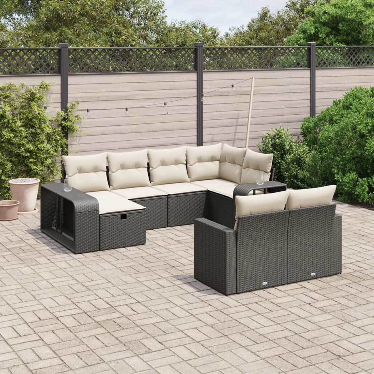 Ein dunkelgraues Outdoor-Ecksofa und Stuhl-Set auf einer Backsteinterrasse. Der Garten hat einen Zaun und Grün.