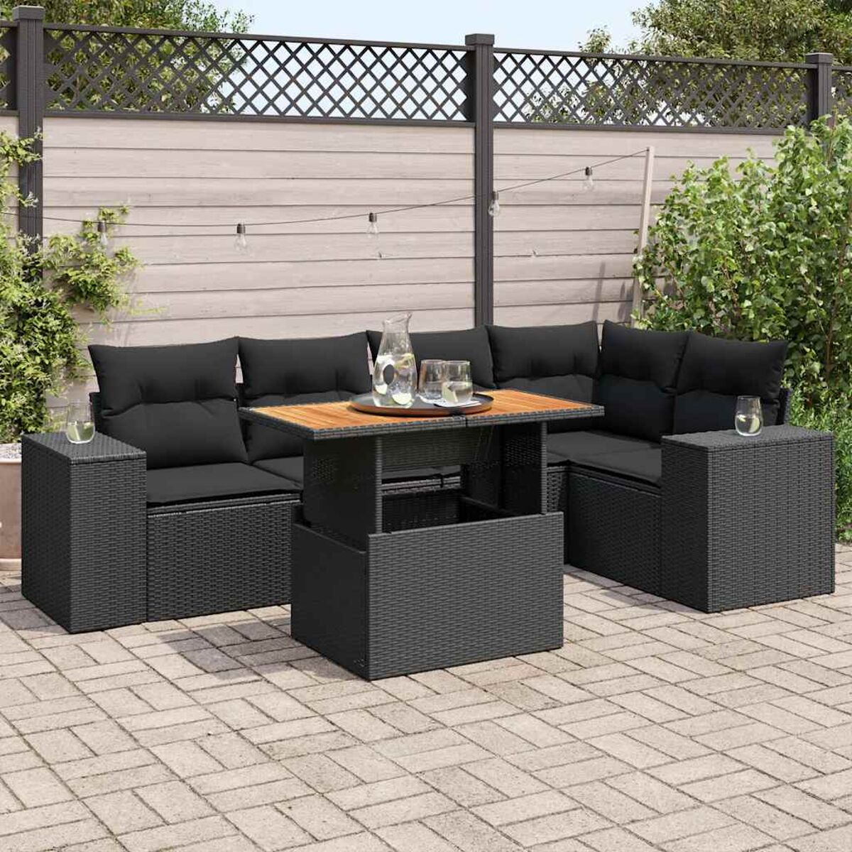 Set da patio esterno con mobili in vimini neri e tavolo in legno. Ci sono bevande e piante sul tavolo.