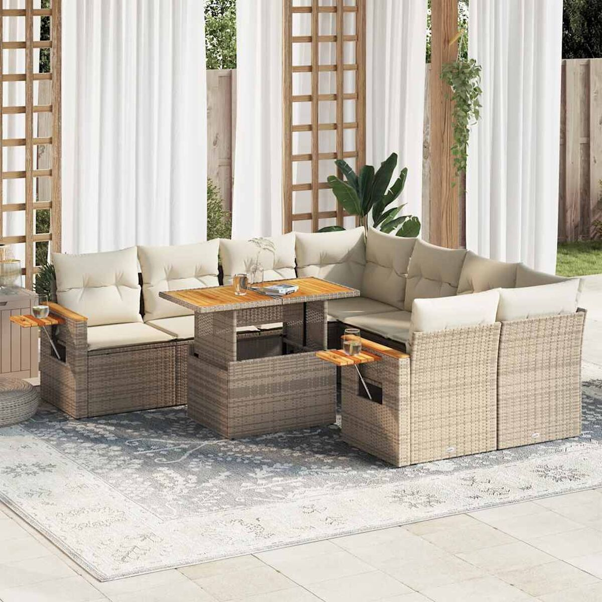 Set di mobili da esterno in vimini con cuscini beige, tavolo in legno e tappeto fantasia. Tende sullo sfondo.