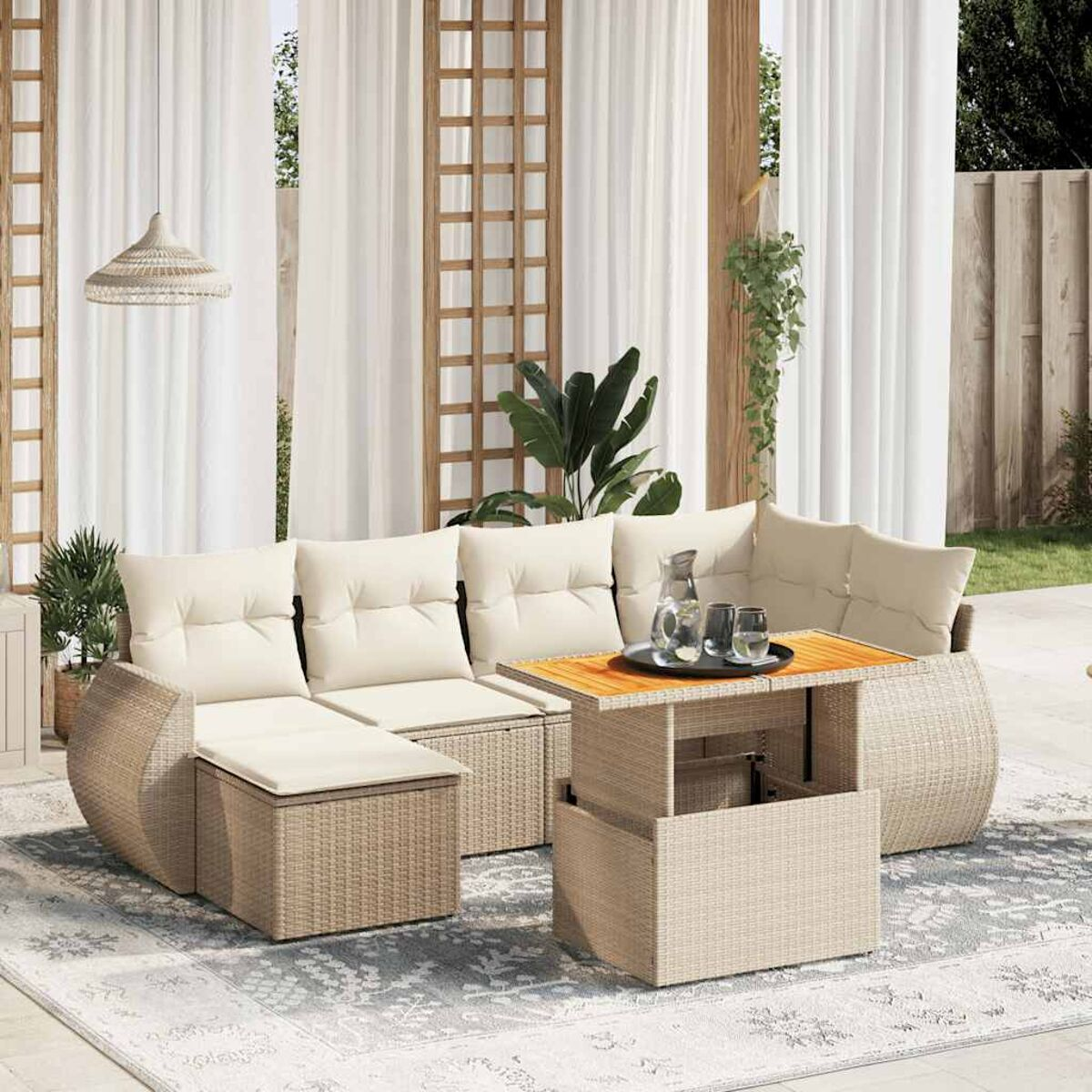Divano in rattan con cuscini, tavolino su tappeto fantasia e tende trasparenti.