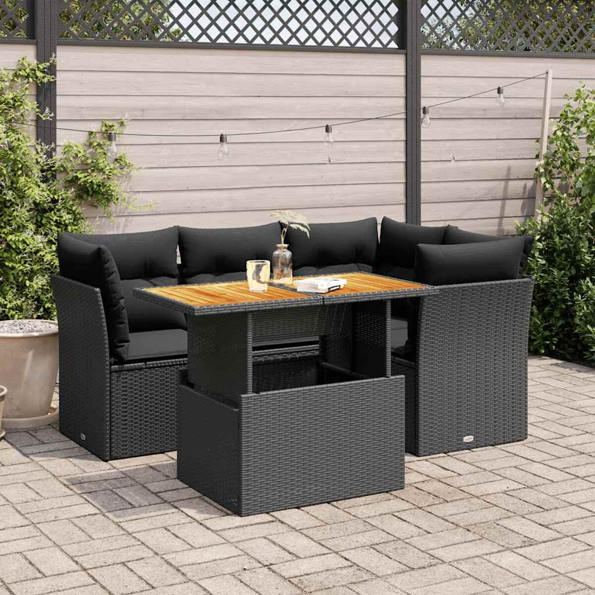 Divano in stile rattan da esterno con cuscini e tavolino. La scena è in un giardino.