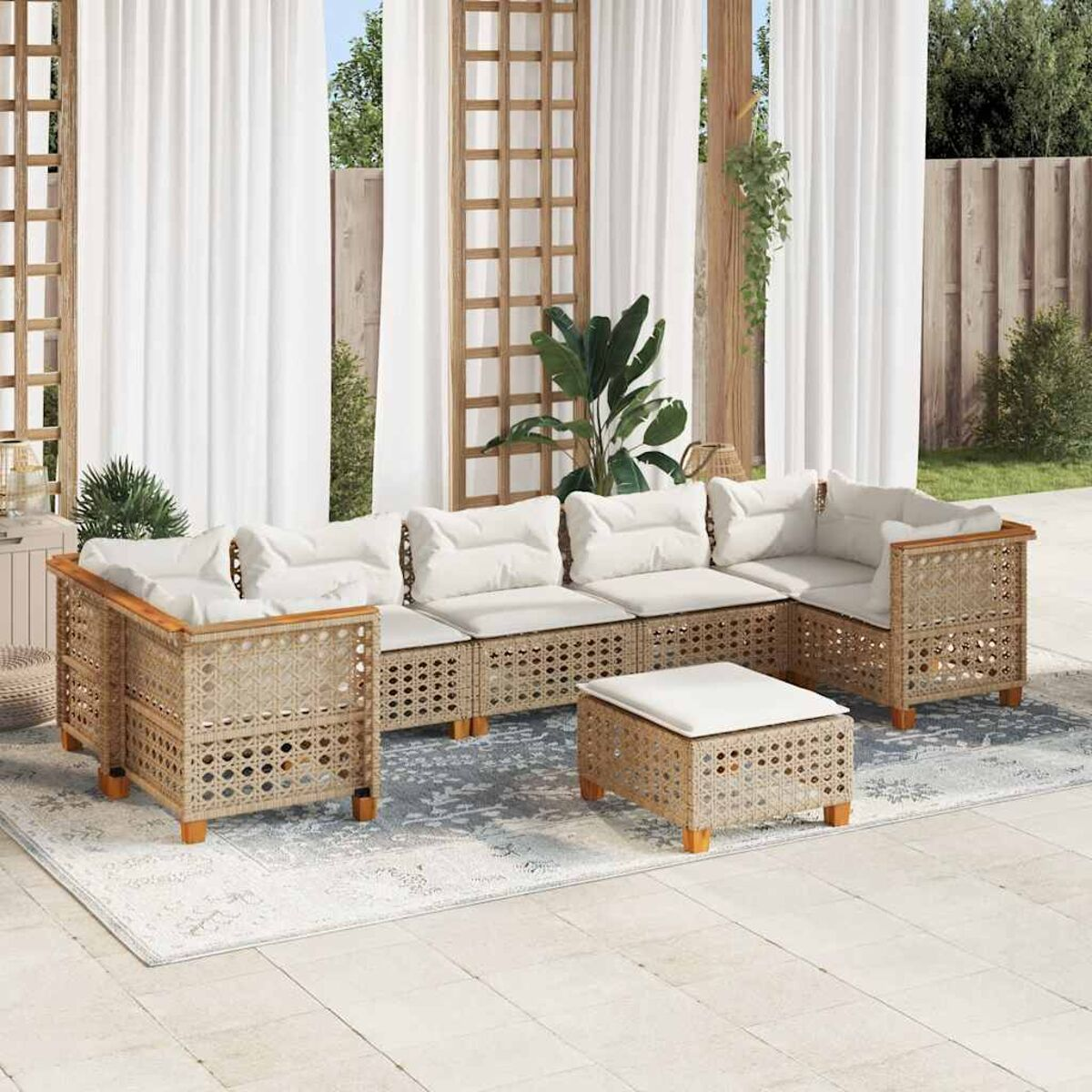 Un divano componibile in rattan beige con cuscini color crema, su un tappeto, con sfondo patio.