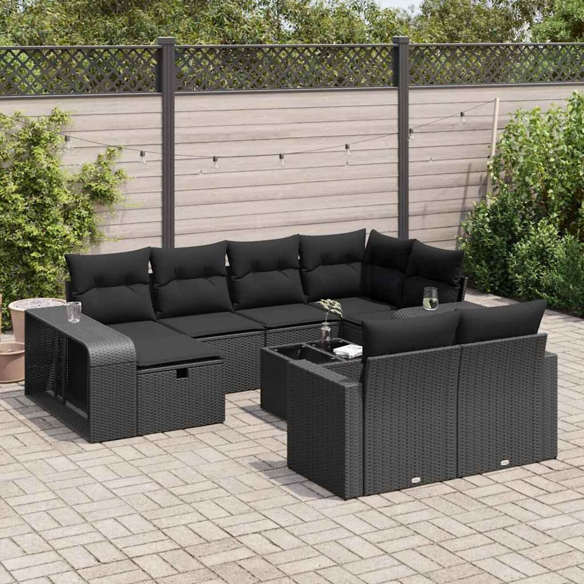 Terrassengarnitur mit schwarzen Korbsesseln und schwarzen Kissen. Enthält einen Couchtisch. Ziegelpflaster.