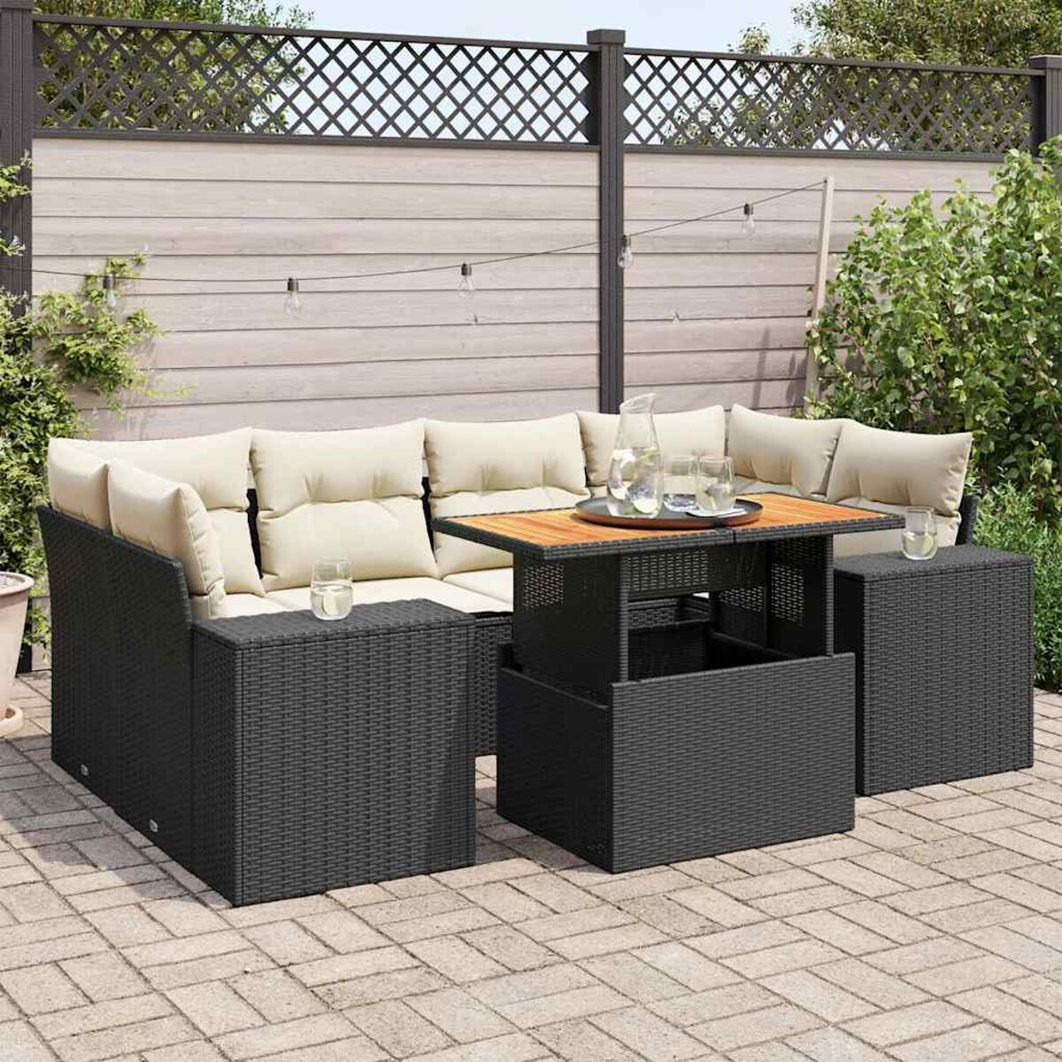 Zona salotto all'aperto con un divano angolare in rattan scuro, un tavolo e un patio in mattoni decorati.