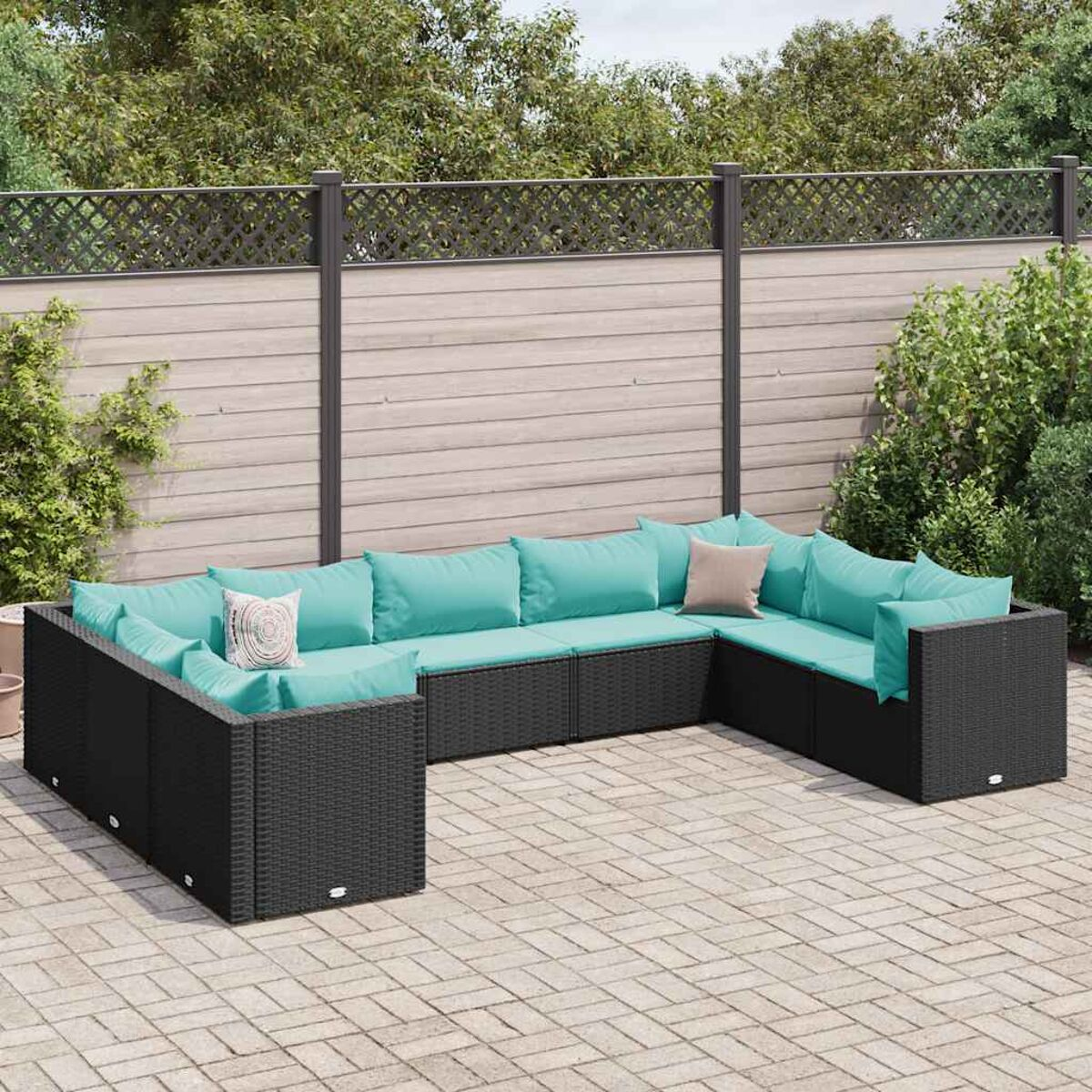 Divano a U in vimini nero con cuscini turchesi su patio pavimentato. Recinzione e fogliame sullo sfondo.