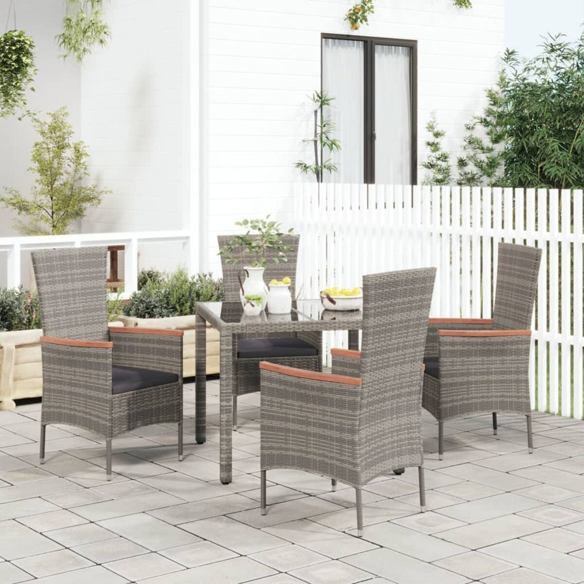 Ein Terrassenset mit vier Stühlen und einem Tisch auf gepflasterter Oberfläche, neben einem weißen Zaun.