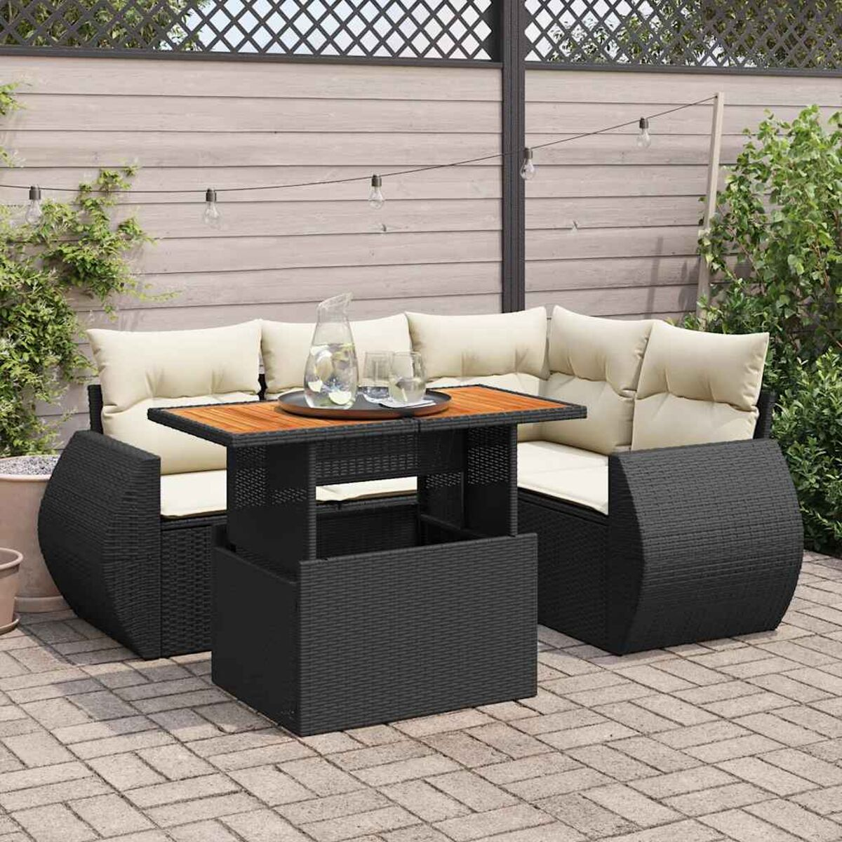 Set divano in vimini nero da esterno con tavolo rialzabile, con cuscini, su un patio in mattoni. Bevande sul tavolo.