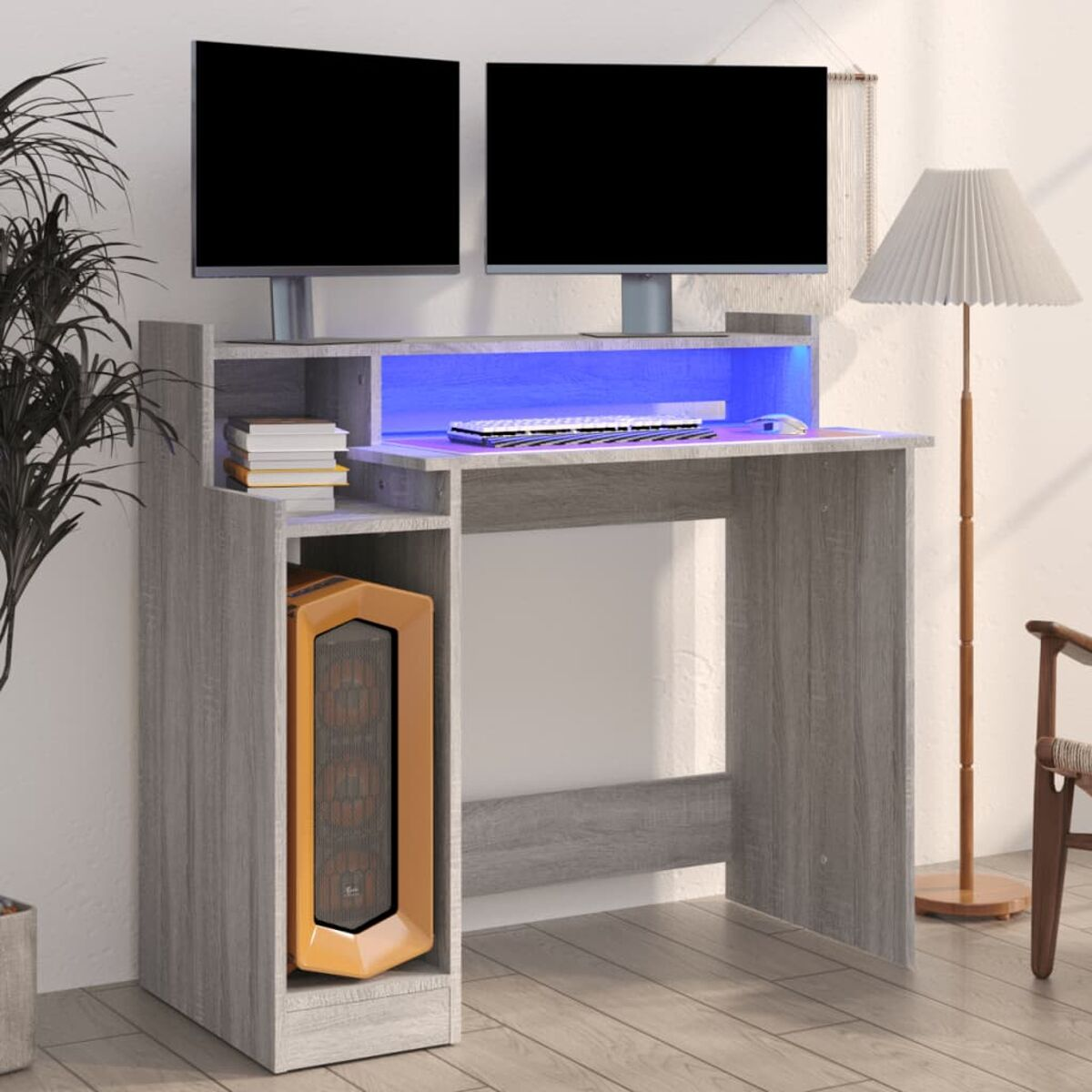 Ein grauer Computertisch mit Monitoren, Tastatur und PC vor weißer Wand.