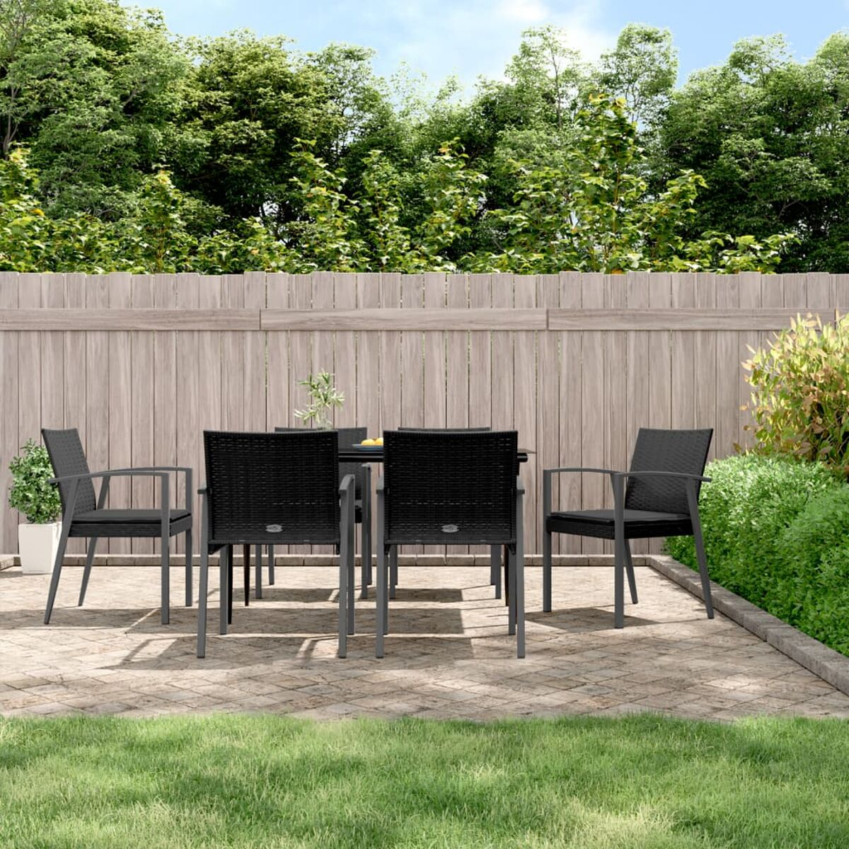 Outdoor-Terrassenset mit schwarzem Tisch, Stühlen und Grün mit Holzzaun im Hintergrund.