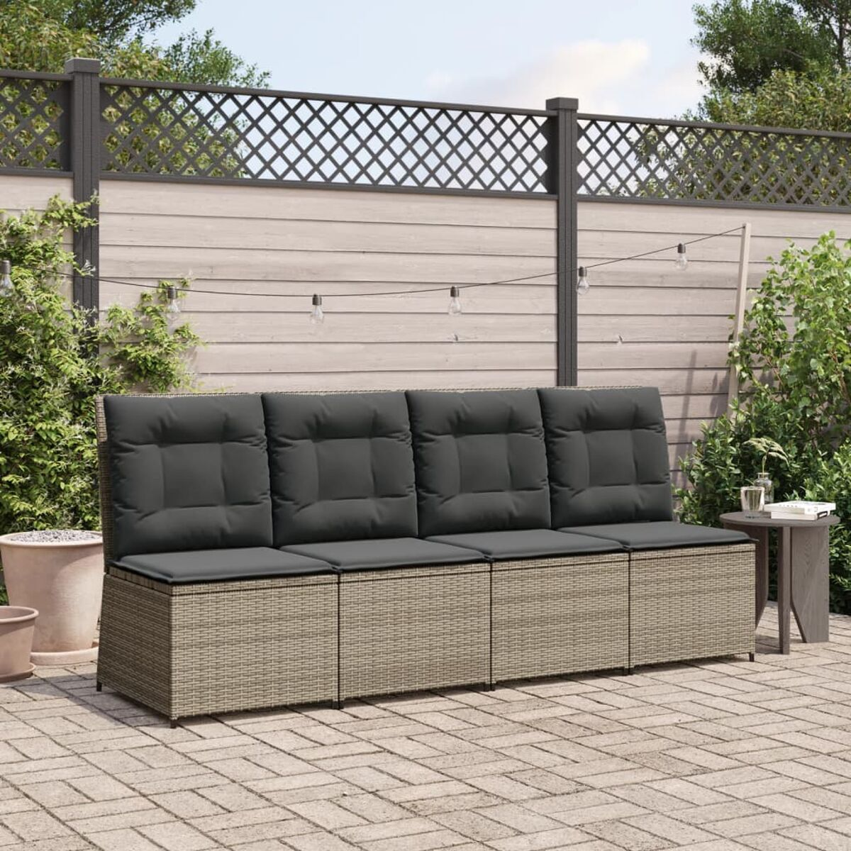 Outdoor-Wickersofa mit grauen Kissen auf einer Ziegelterrasse. Zaun, Pflanzen und Beistelltisch sind sichtbar.