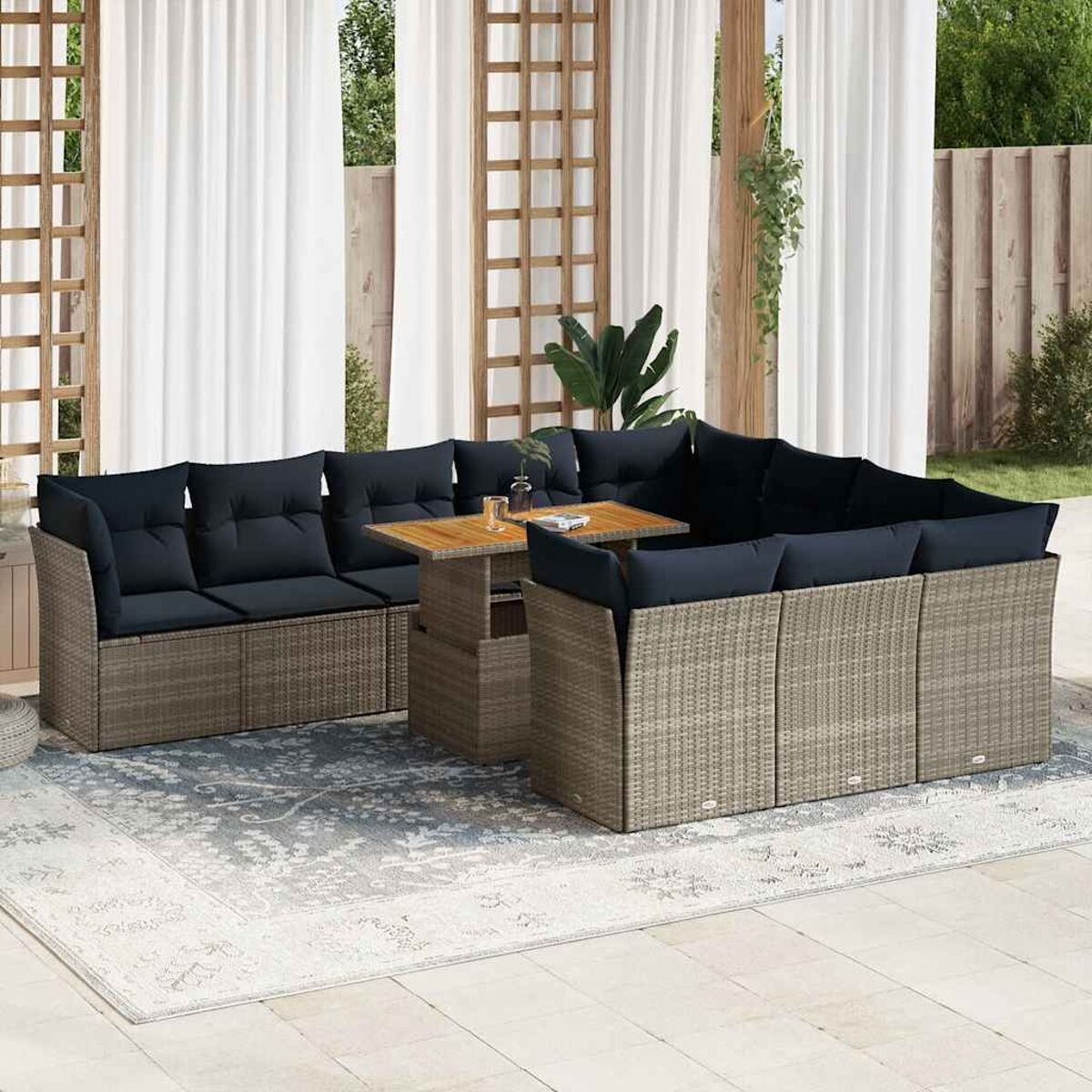 Divano componibile in rattan con cuscini neri e tavolo in legno su tappeto. Finestra e tende dietro.