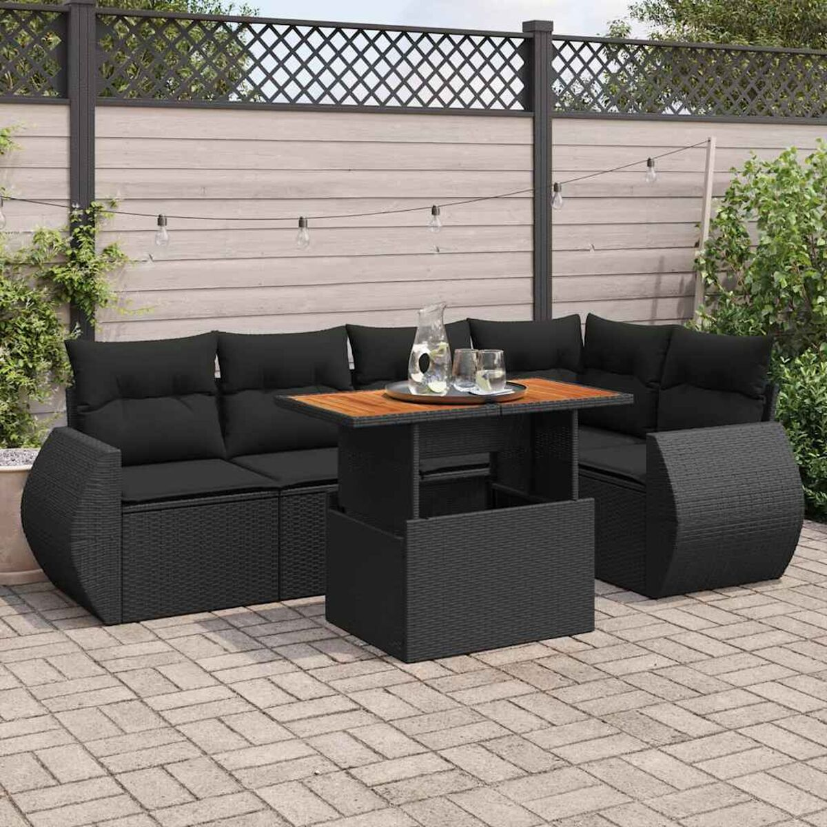 Set divano in vimini nero per esterni con cuscini, tavolo, bicchieri e giardino.