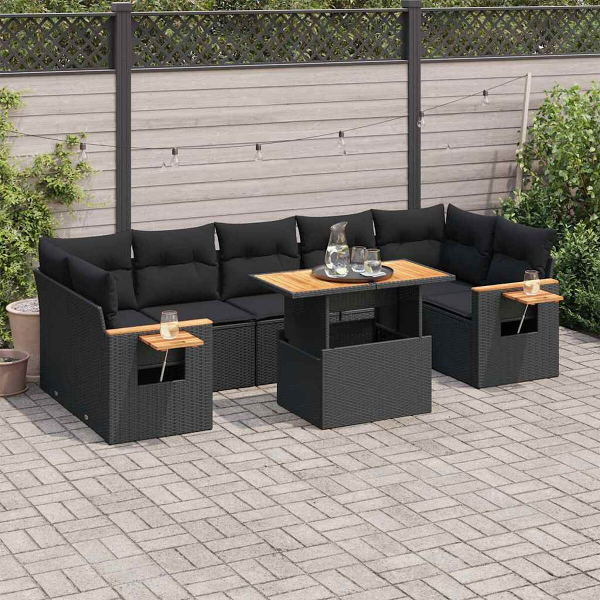 Set divani in rattan nero da esterno con tavolino in legno. Cuscini neri. Patio in mattoni.