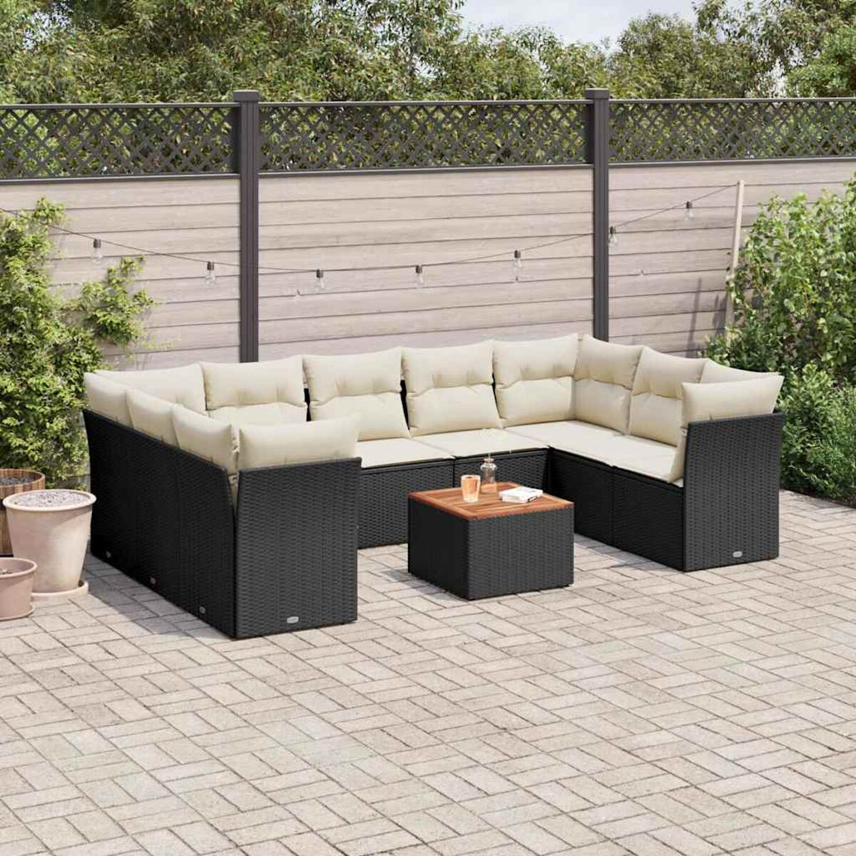 Schwarzes Rattan-Ecksofa mit cremefarbenen Kissen und einem kleinen Tisch auf einer Ziegelterrasse.