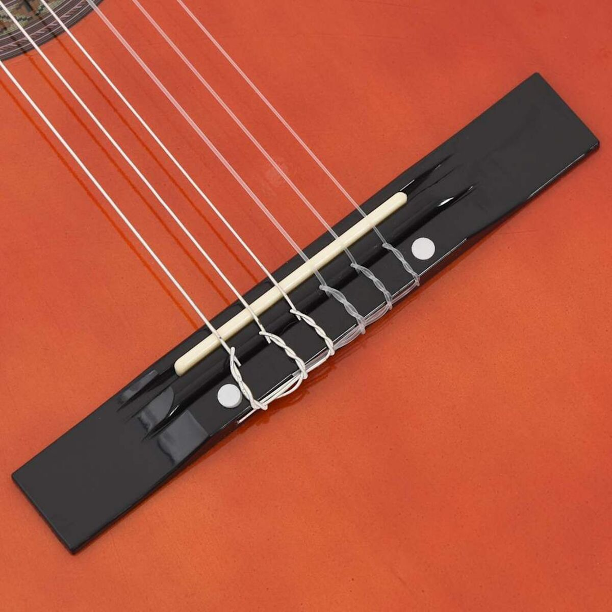 Nahaufnahme eines Gitarrenstegs mit Saiten. Der Steg ist schwarz und die Gitarre ist orange.