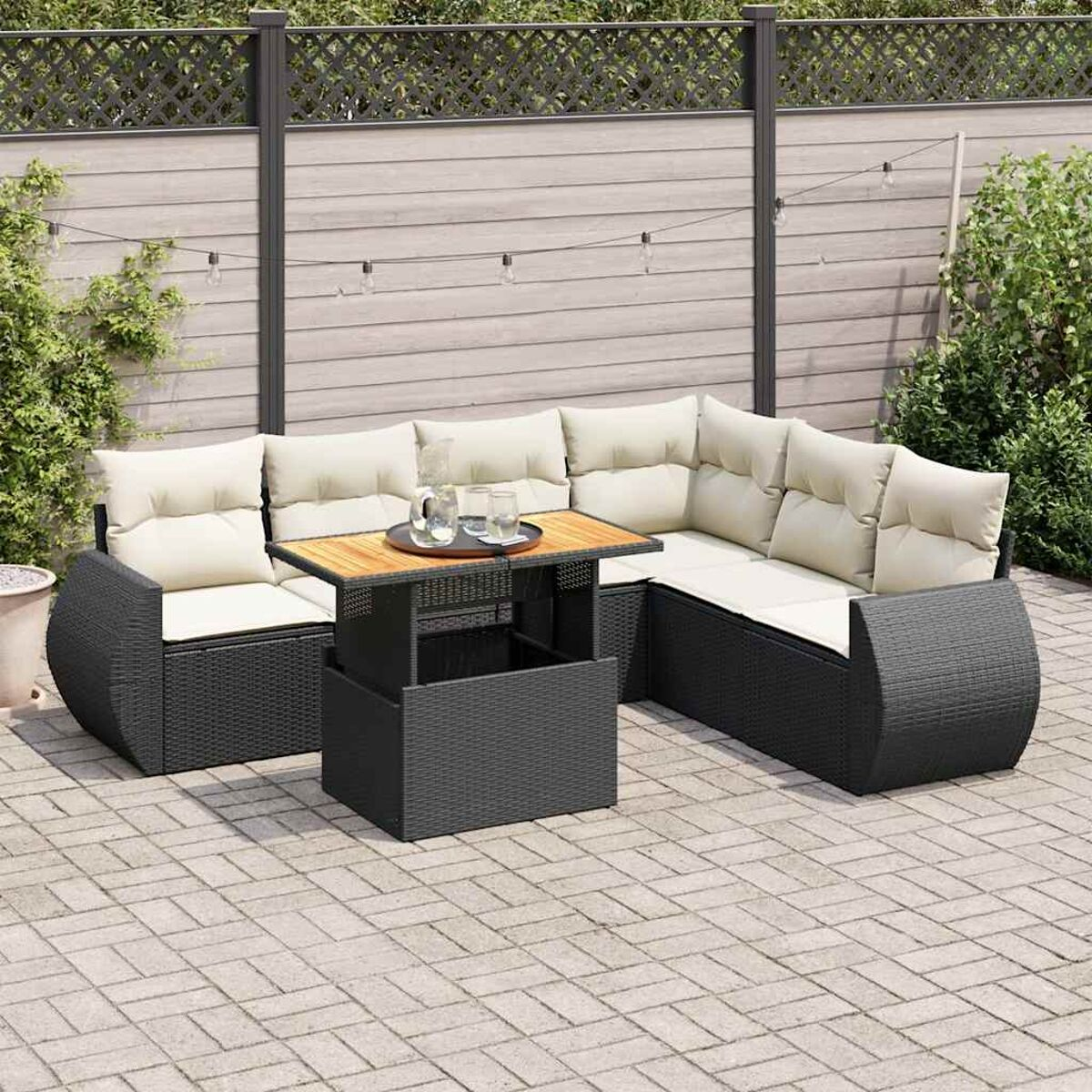 Set divano in vimini nero per esterni con cuscini crema, tavolo e decorazioni in giardino.