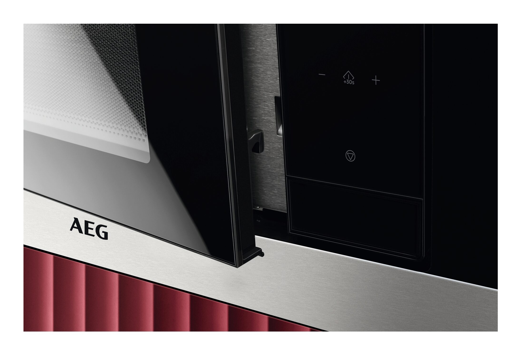 Kuchenka mikrofalowa AEG, otwarte drzwi, czarny szklany front, srebrne wykończenie, czerwone tło.
