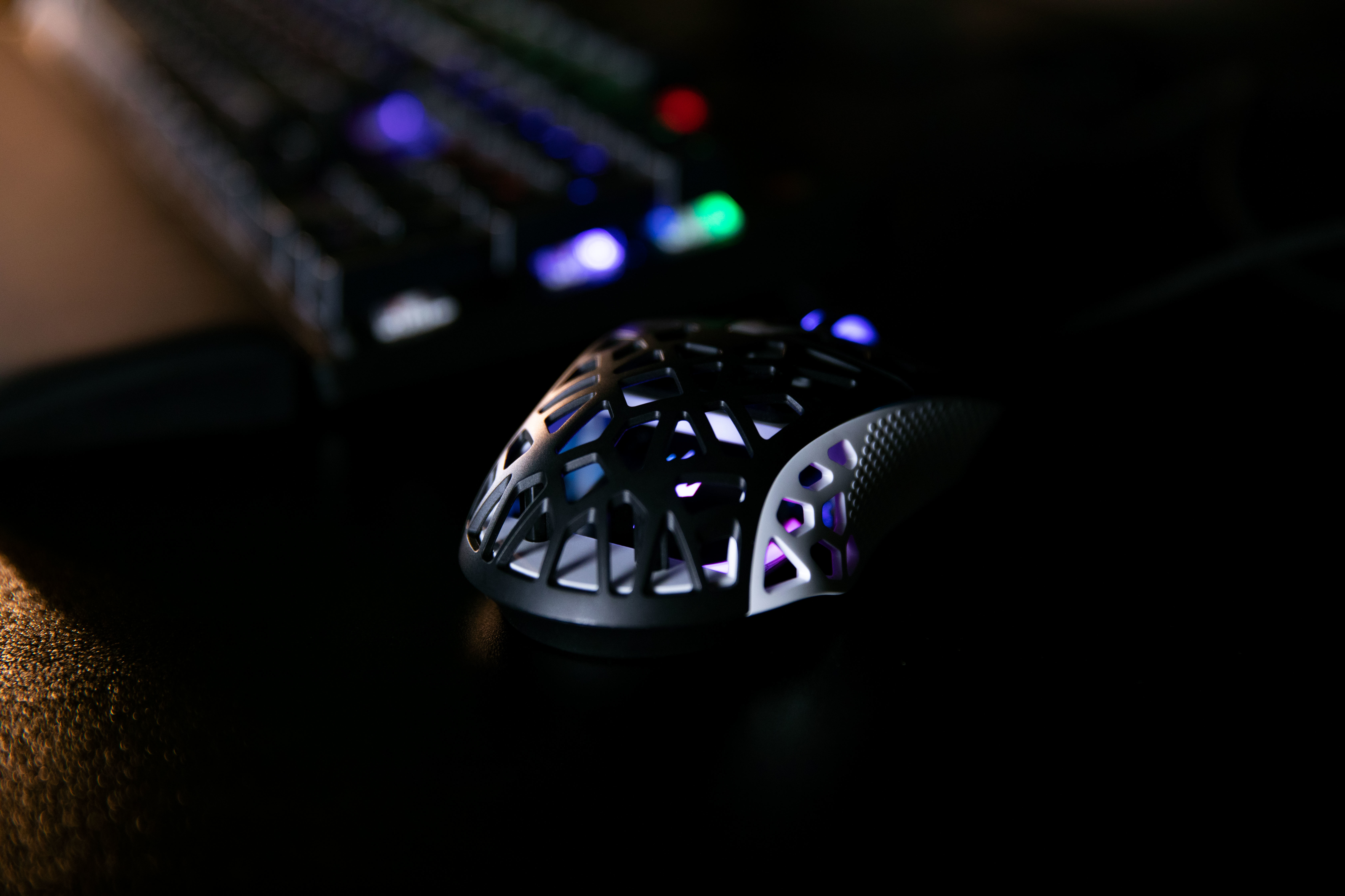 Czarna mysz gamingowa o wzorze plastra miodu z podświetleniem RGB. Mysz jest na czarnej powierzchni.