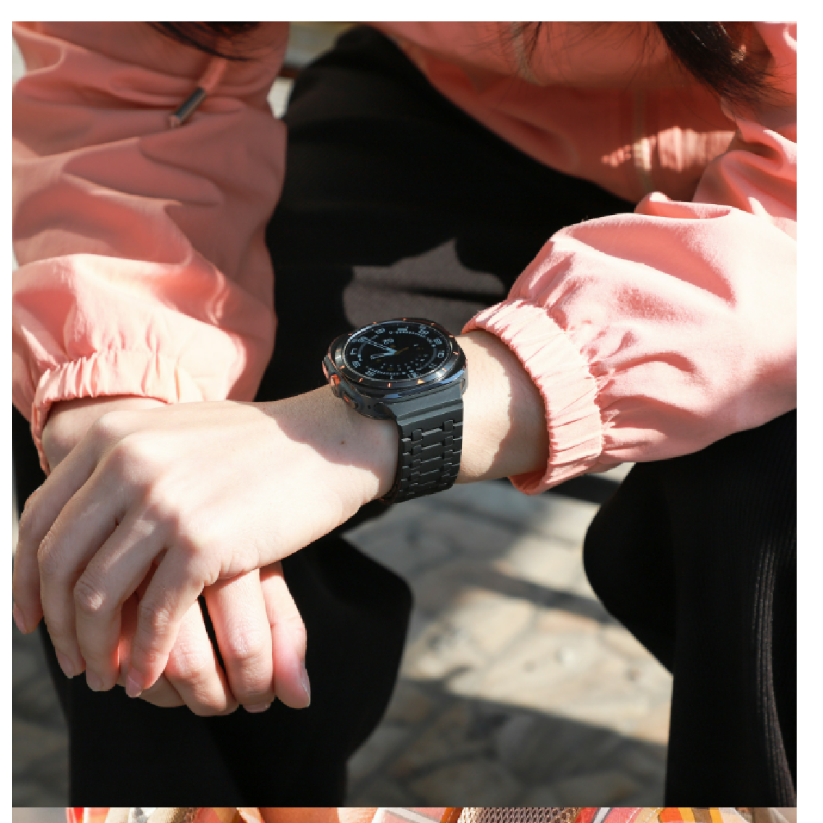 Polso di una persona con orologio e braccialetto neri. La persona indossa una camicia color pesca.