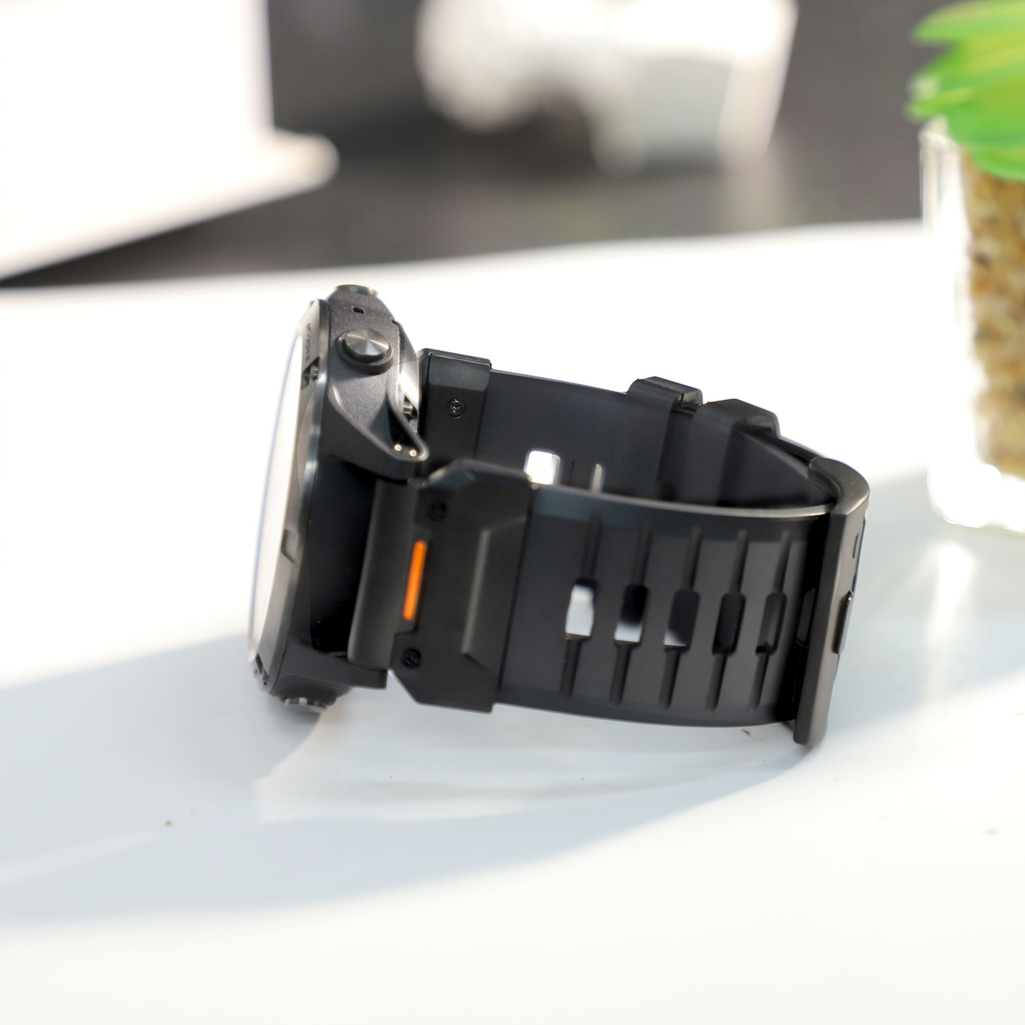 Eine schwarze Smartwatch auf einer weißen Oberfläche. Das Uhrenarmband ist schwarz, der Hintergrund unscharf.