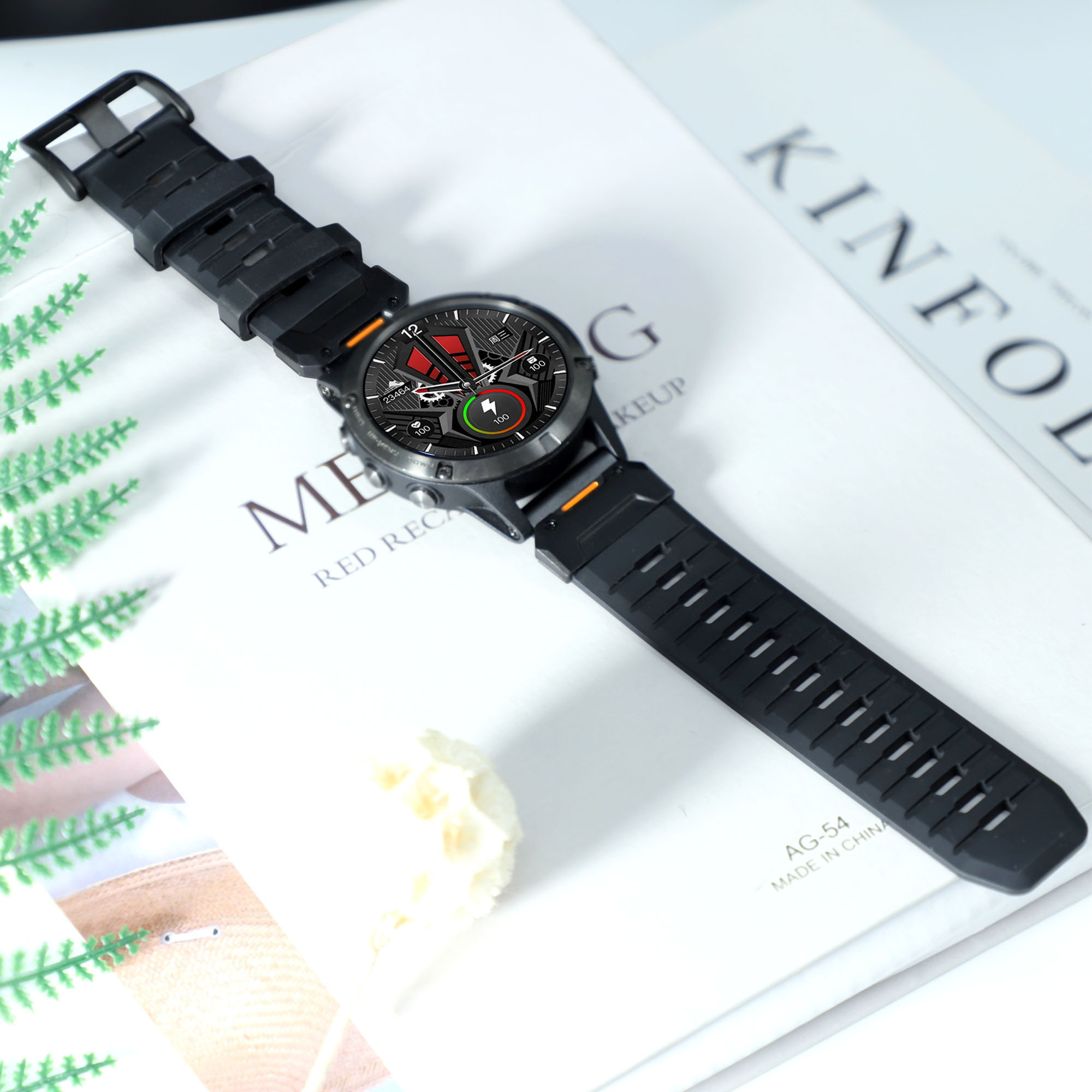 Schwarze Smartwatch auf einem Buch, mit Blatt und Blumen. Weißer Hintergrund.