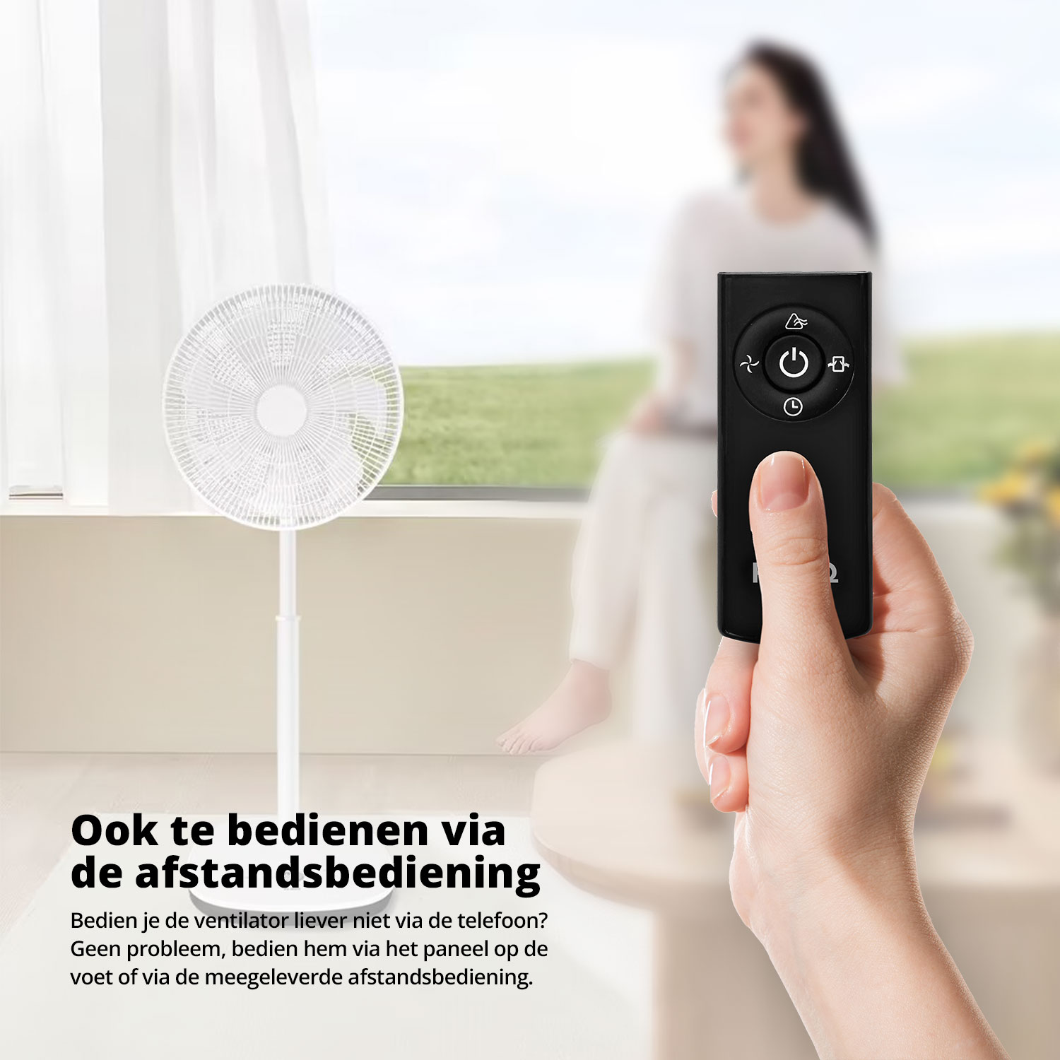 Une main tenant une télécommande noire avec un ventilateur blanc en arrière-plan.