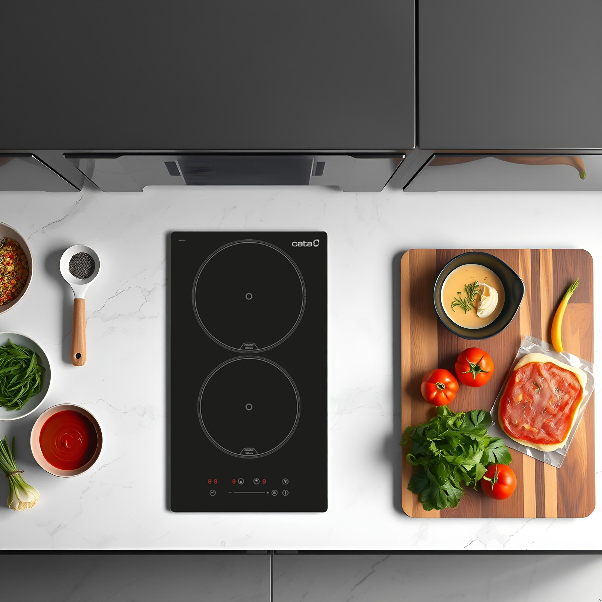 Vista superior de una placa de inducción negra con dos fuegos y artículos de cocina sobre encimera de mármol.