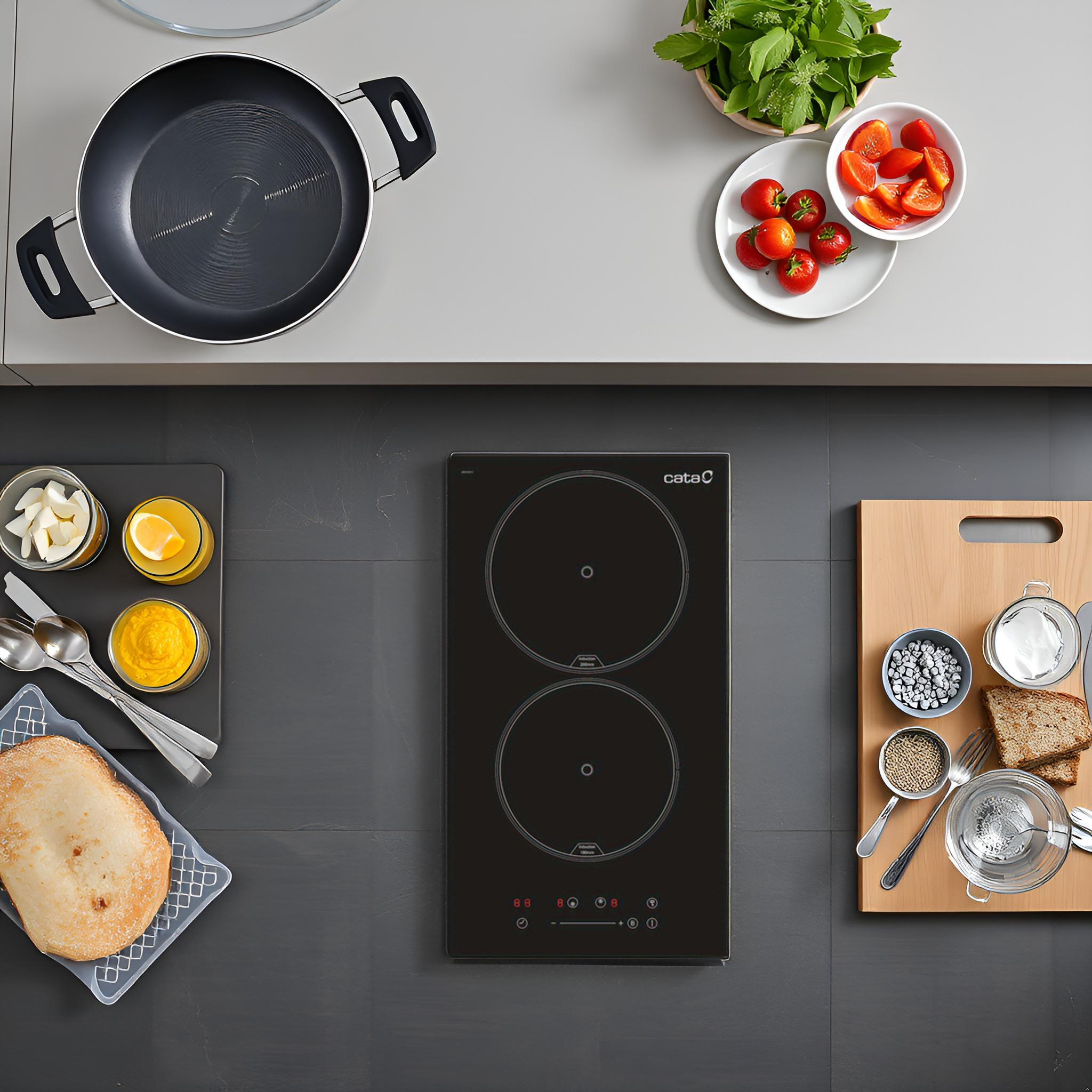 Vista superior de encimera de cocina con placa de inducción negra, ingredientes y utensilios.