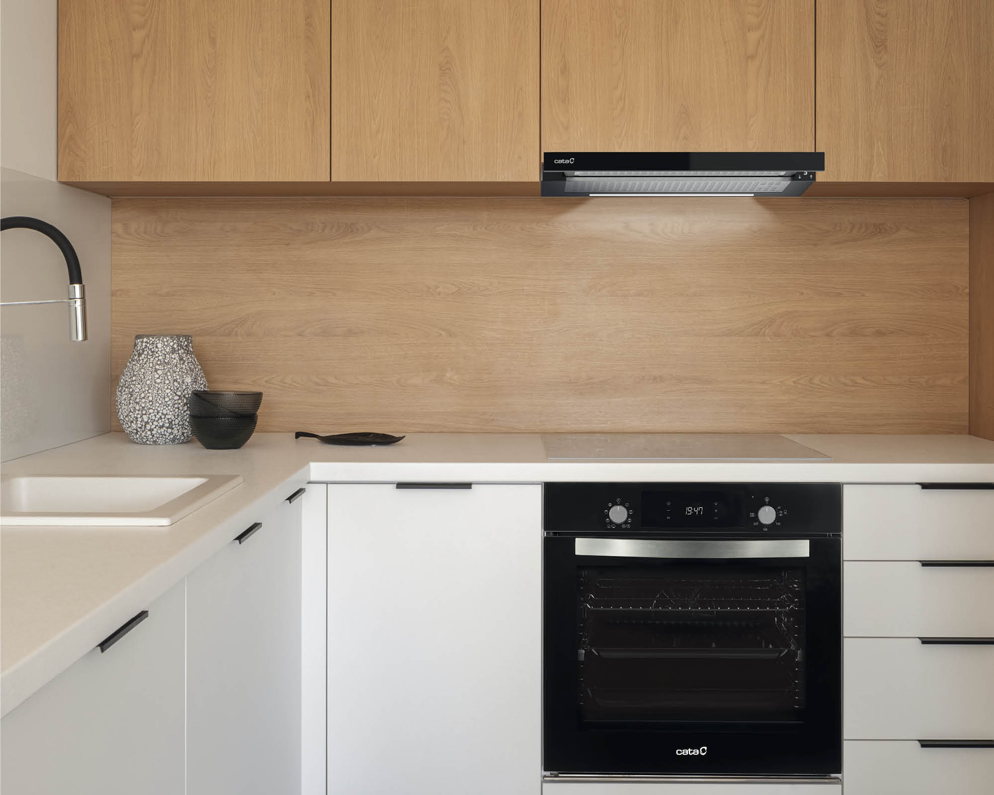 Cocina moderna con armarios blancos, salpicadero de madera y horno y campana negros. Decoración en la encimera.