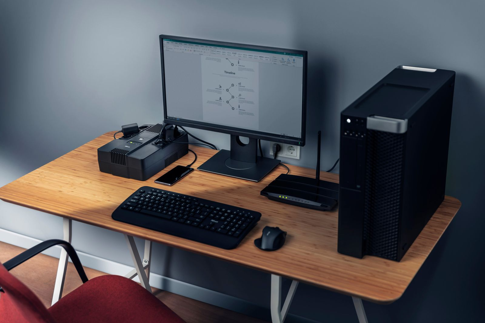 Escritorio con monitor, torre de PC, teclado, ratón, router y teléfono.