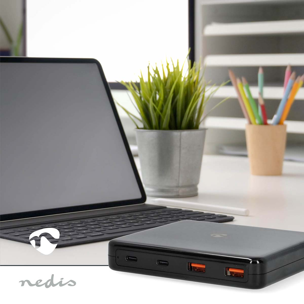 Power bank nero con porte arancioni, vicino a laptop e pianta.