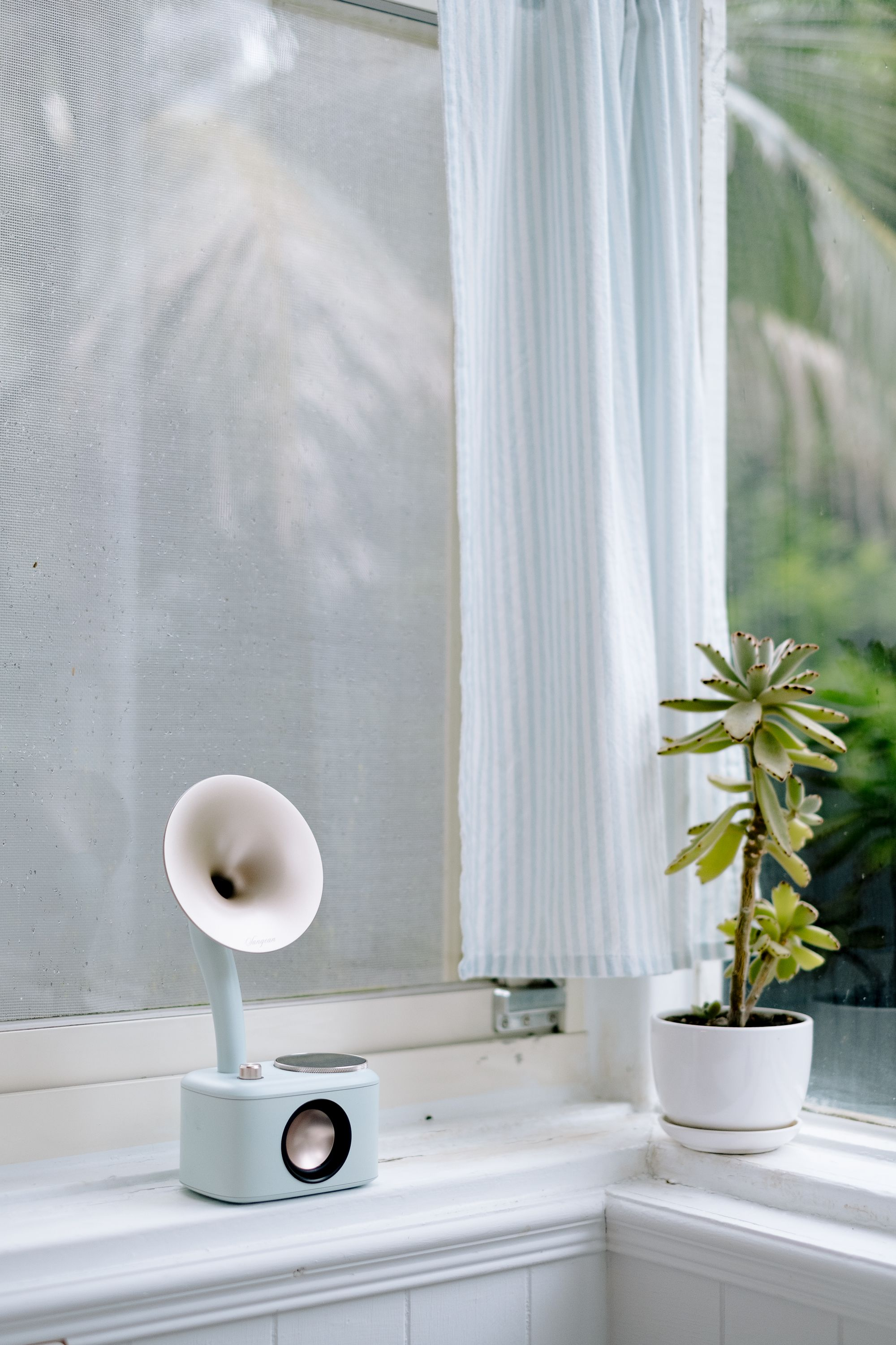 Głośnik w stylu vintage na parapecie. Jasnoniebieski z dużą tubą. Roślina i zasłony w tle.